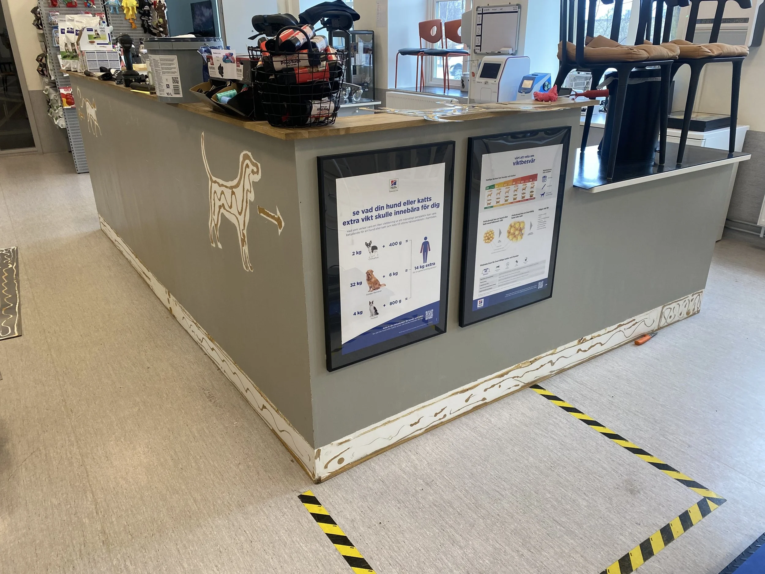 En butikskassa med informationstavlor, några höga pallstolar staplade ovanpå varandra, och en strypsnurra, med en markering på golvet framför.