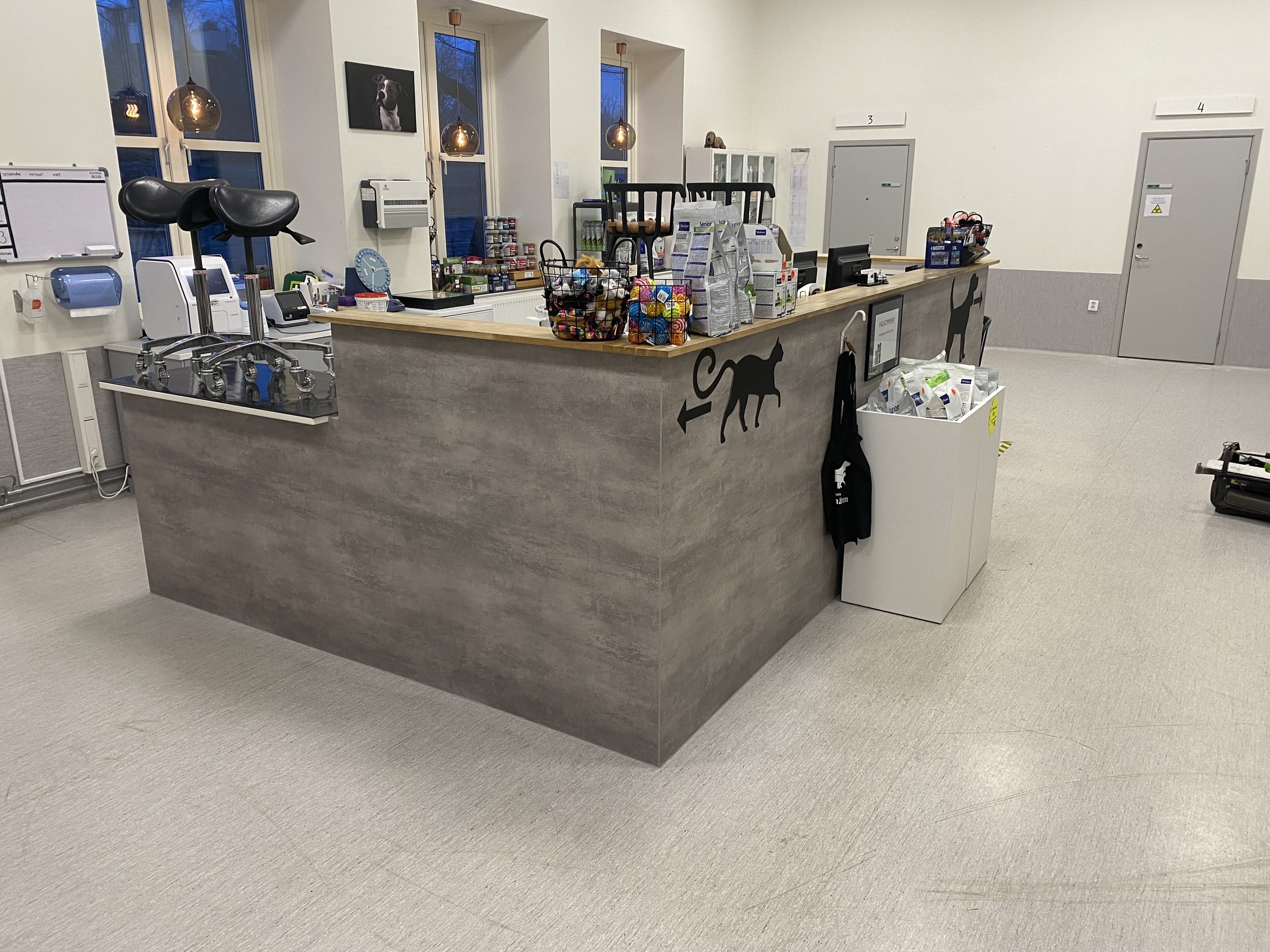 Kassenyta i en djuraffär eller veterinärklinik med olika produkter, kattsymboler och ett svart förkläde hängande på sidan.