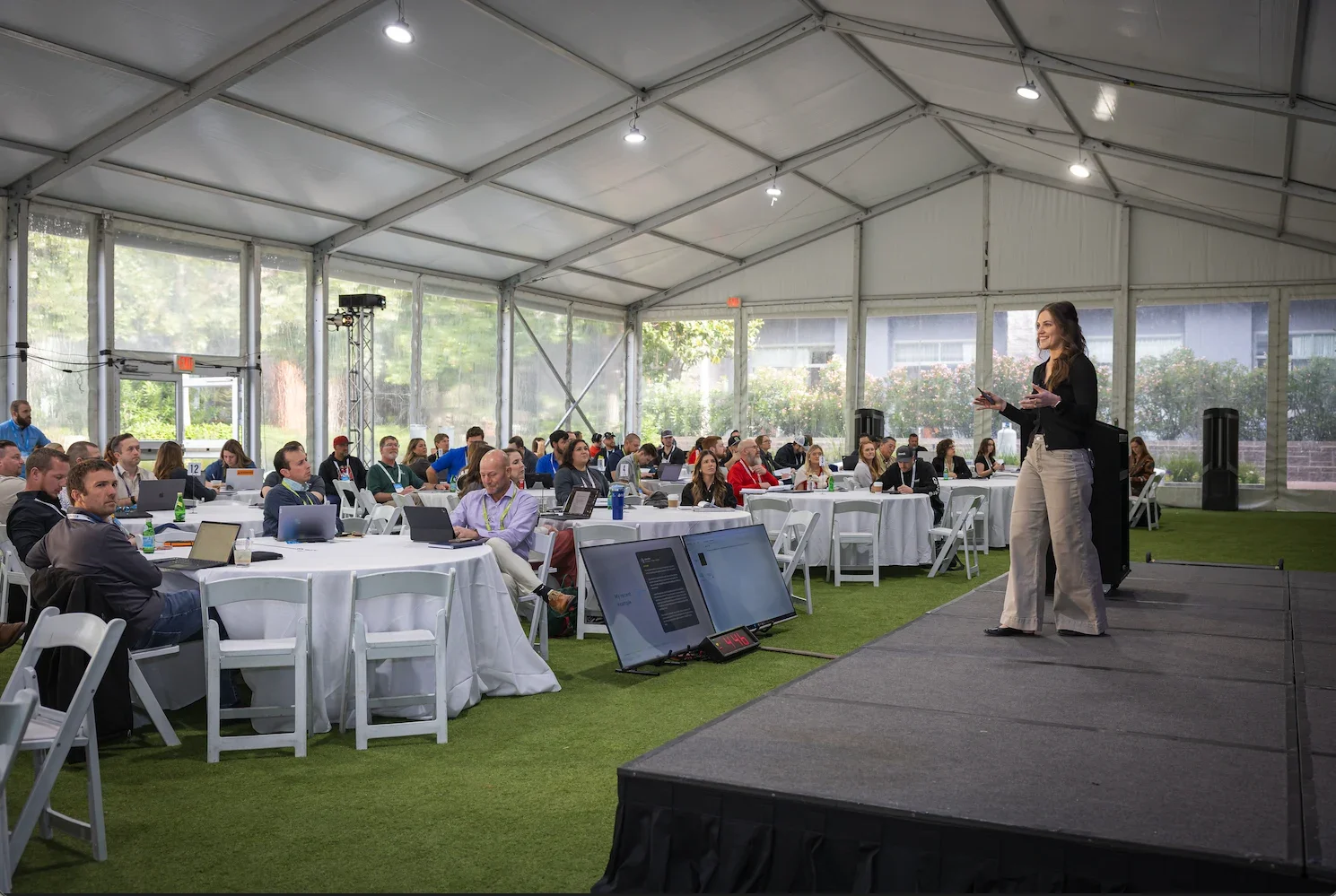 Speaking on stage at LeanScaper event: Jaden Miller presenting on stage to a room of lawn and landscape business owners at a LeanScaper event, with attendees seated at round tables with laptops.