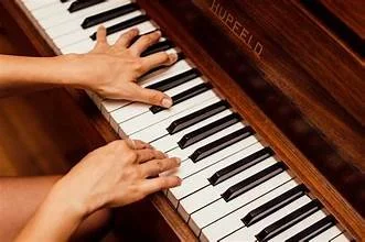 Close-up of hands playing a wooden upright piano with black and white keys.