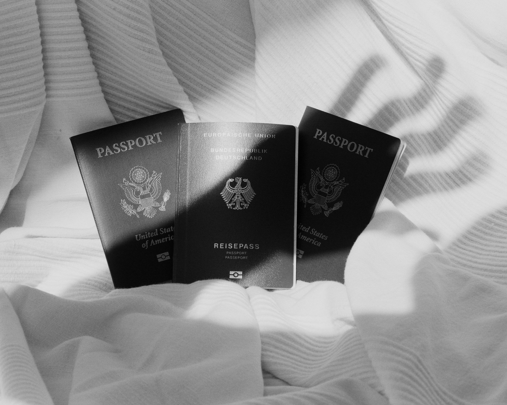 Three passports placed on a textured fabric surface, two are from the United States and one from Germany, with shadows cast on the fabric.