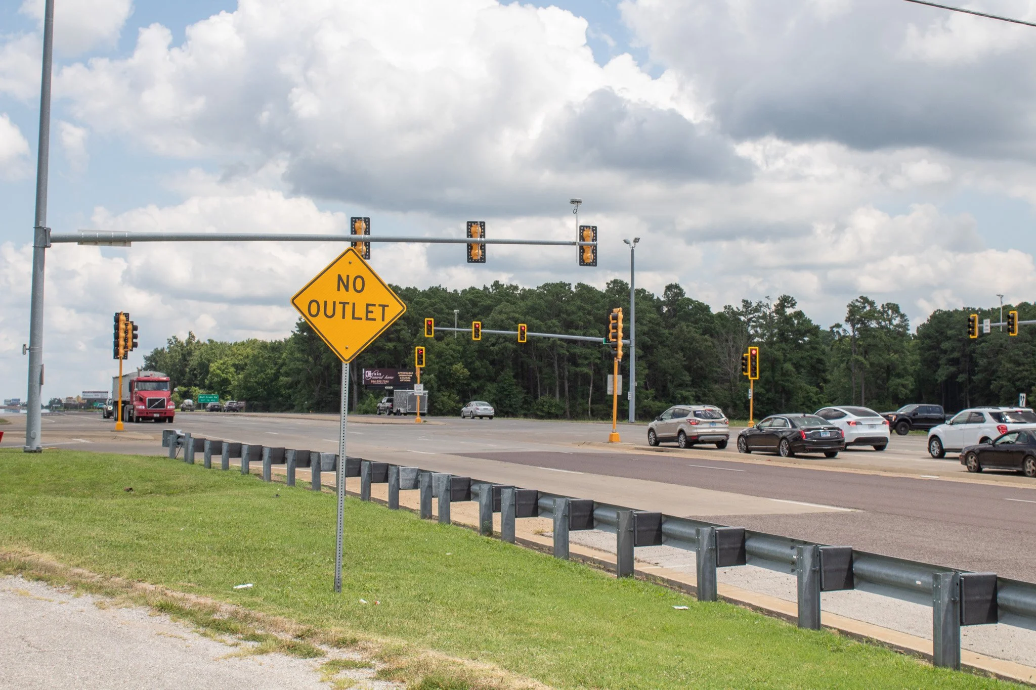 A sign that says "No Outlet" next to a roadway with guardrail