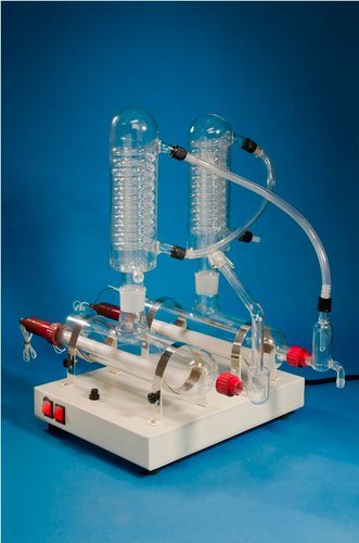 A distillation apparatus with two vertical glass columns connected by tubing, mounted on a white base with control knobs, set against a blue background.
