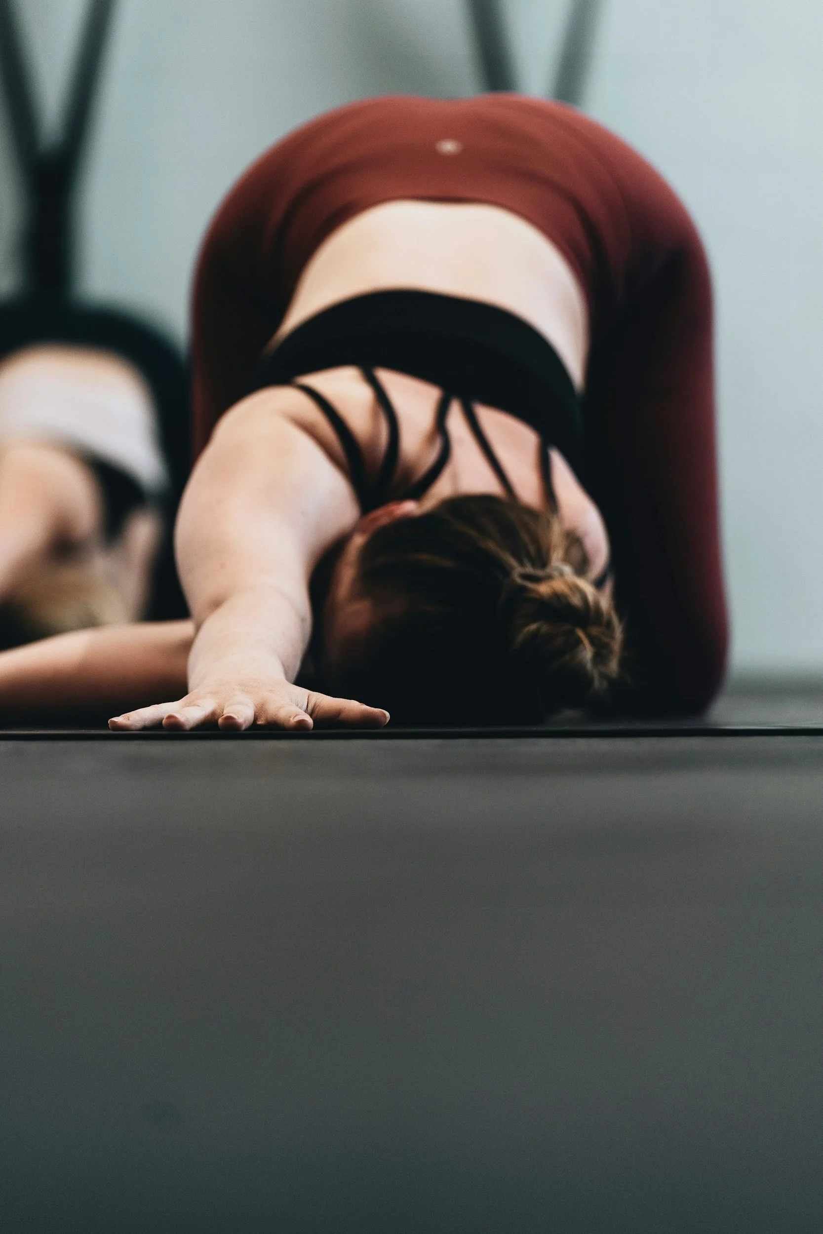 Woman doing a child's pose yoga stretch on a mat in a gym or studio.