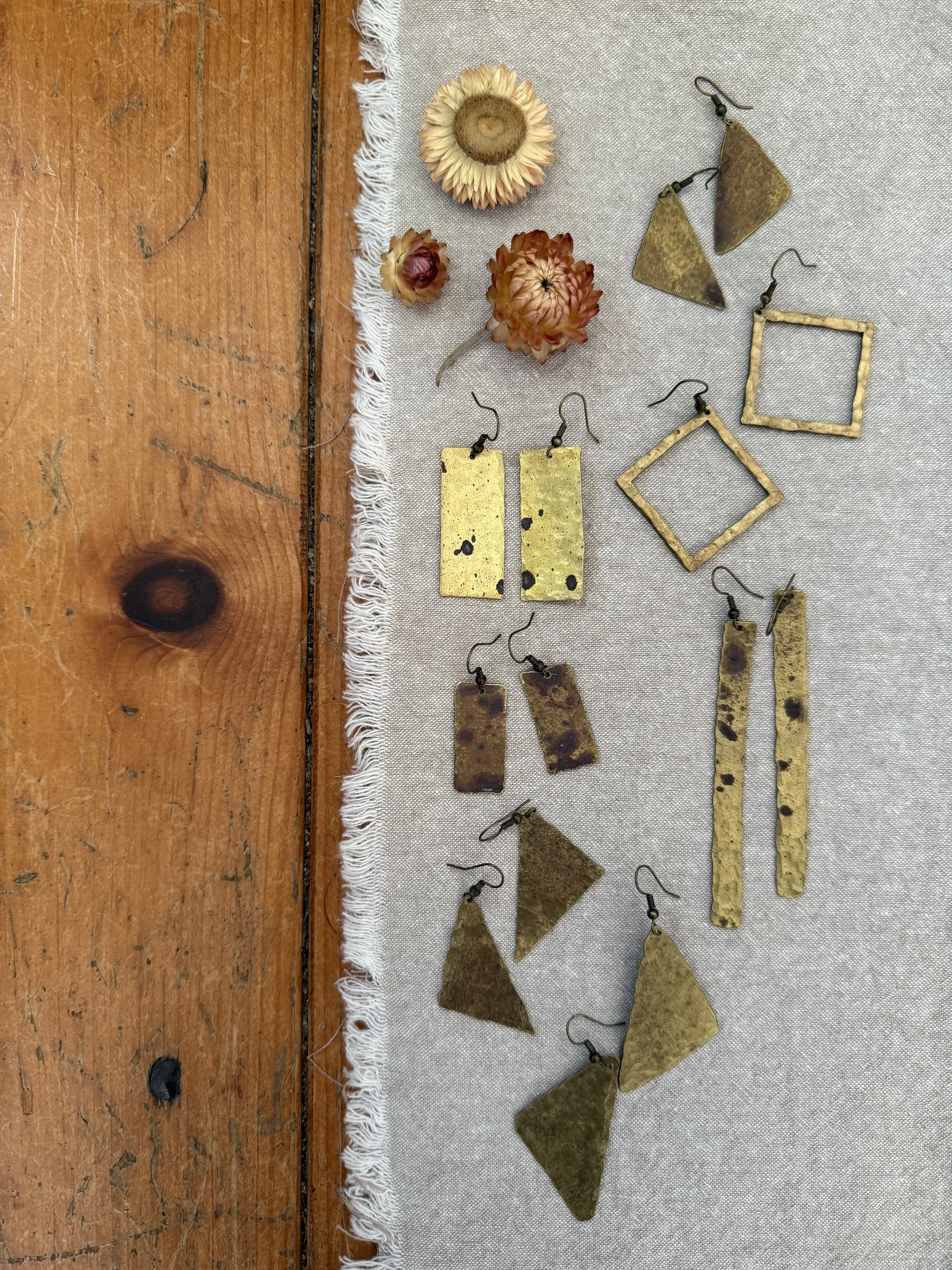 Various handmade jewelry pieces, including earrings and pendants, arranged on a light fabric surface.