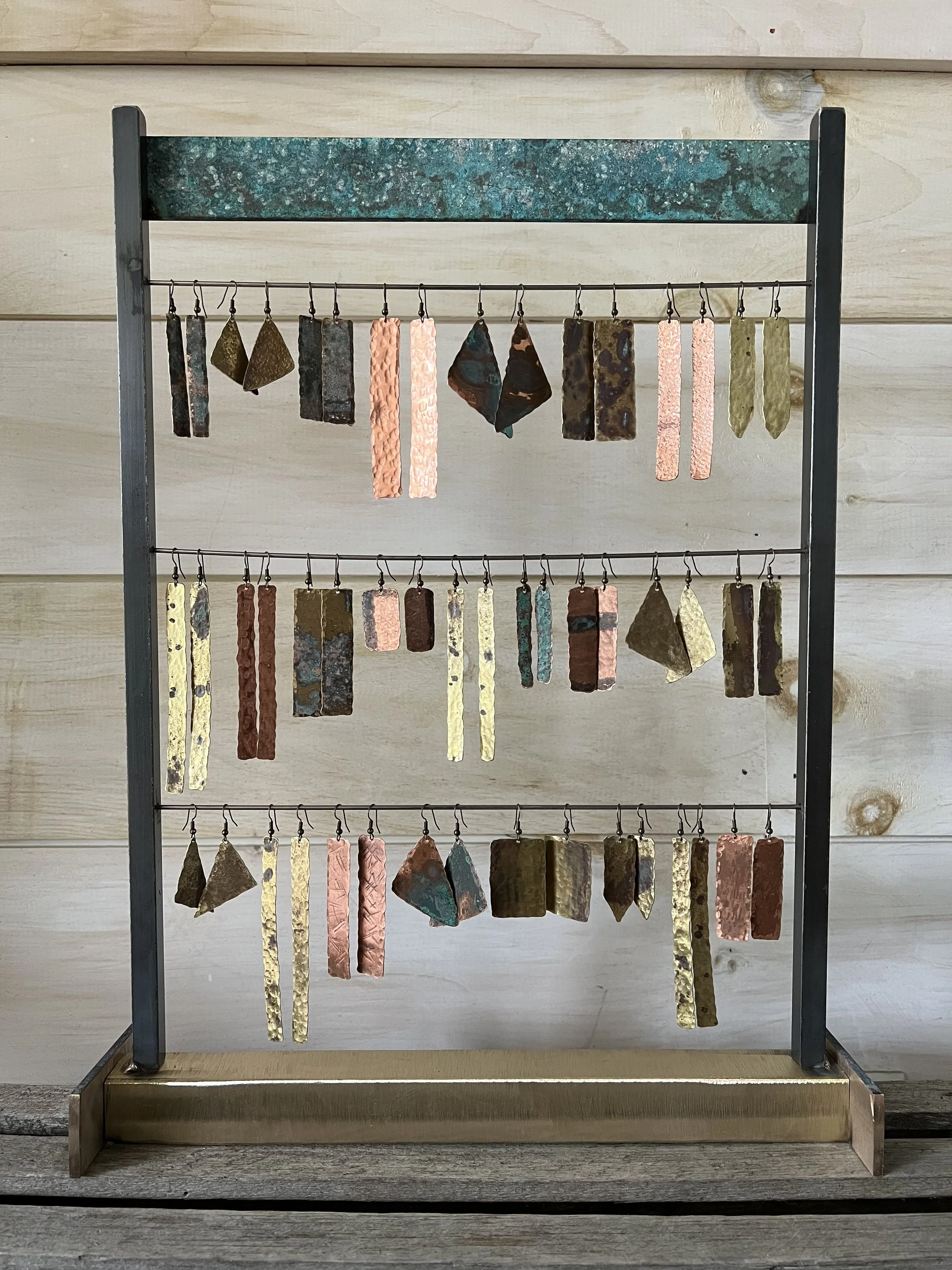 Display of earrings with hanging hooks, arranged on a multi-tiered stand against a wooden wall.
