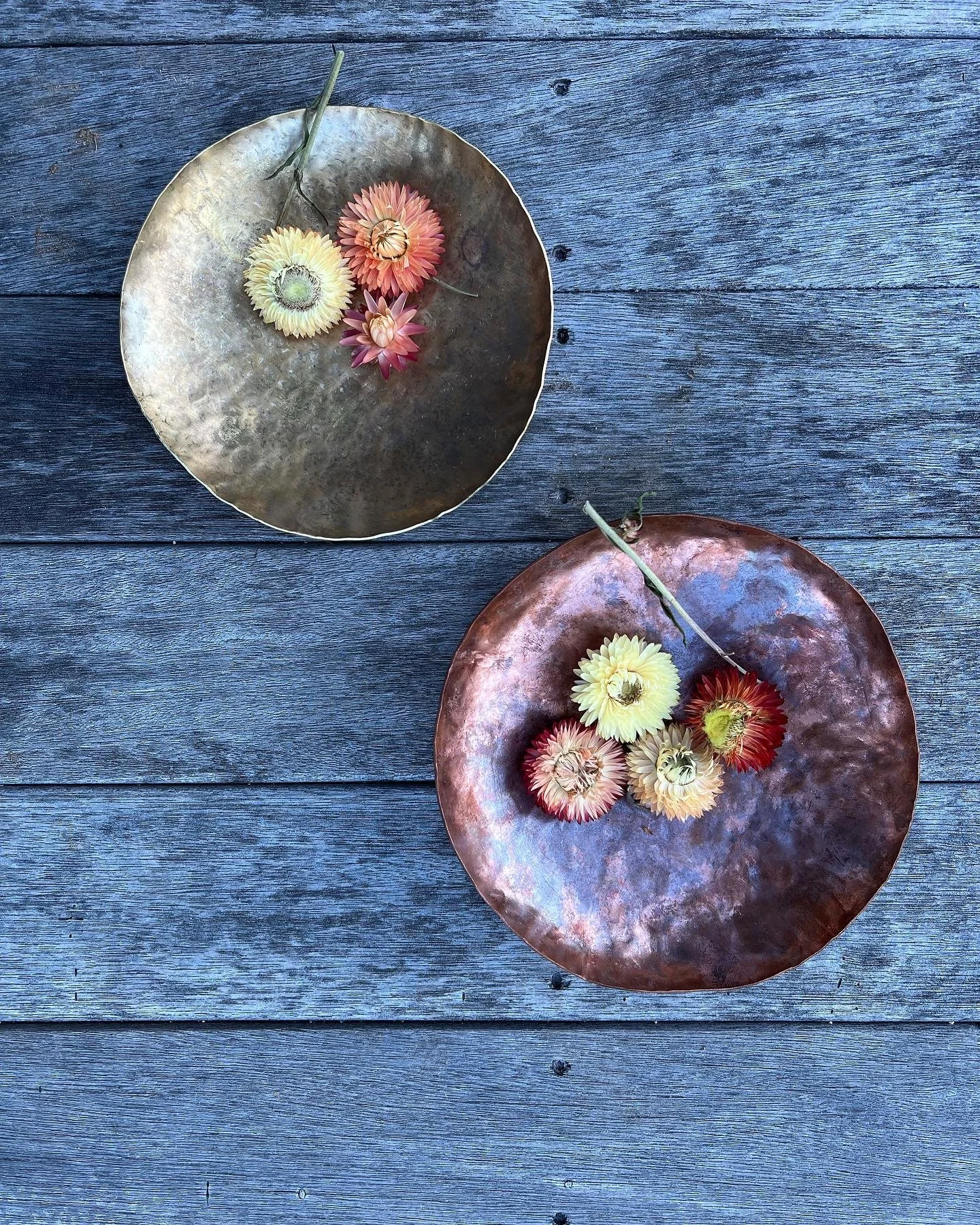 Two metal trays with dried flowers placed on a weathered wooden surface.