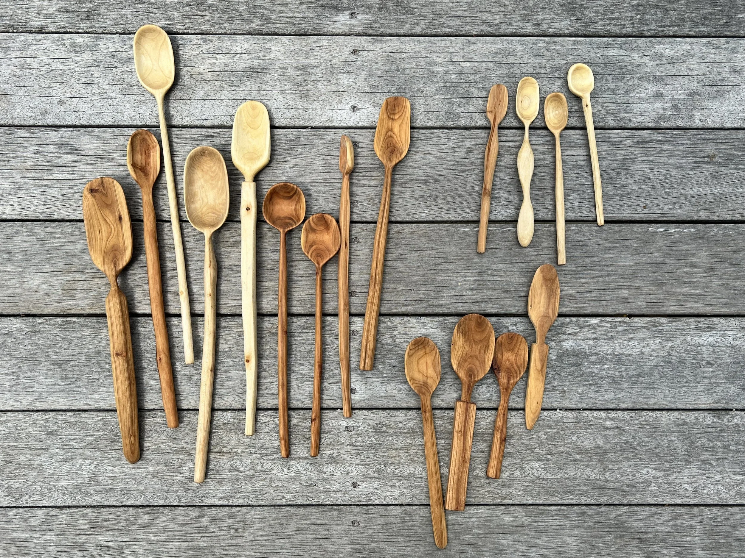 Collection of wooden spoons of various sizes and shapes laid out on a gray wooden surface.