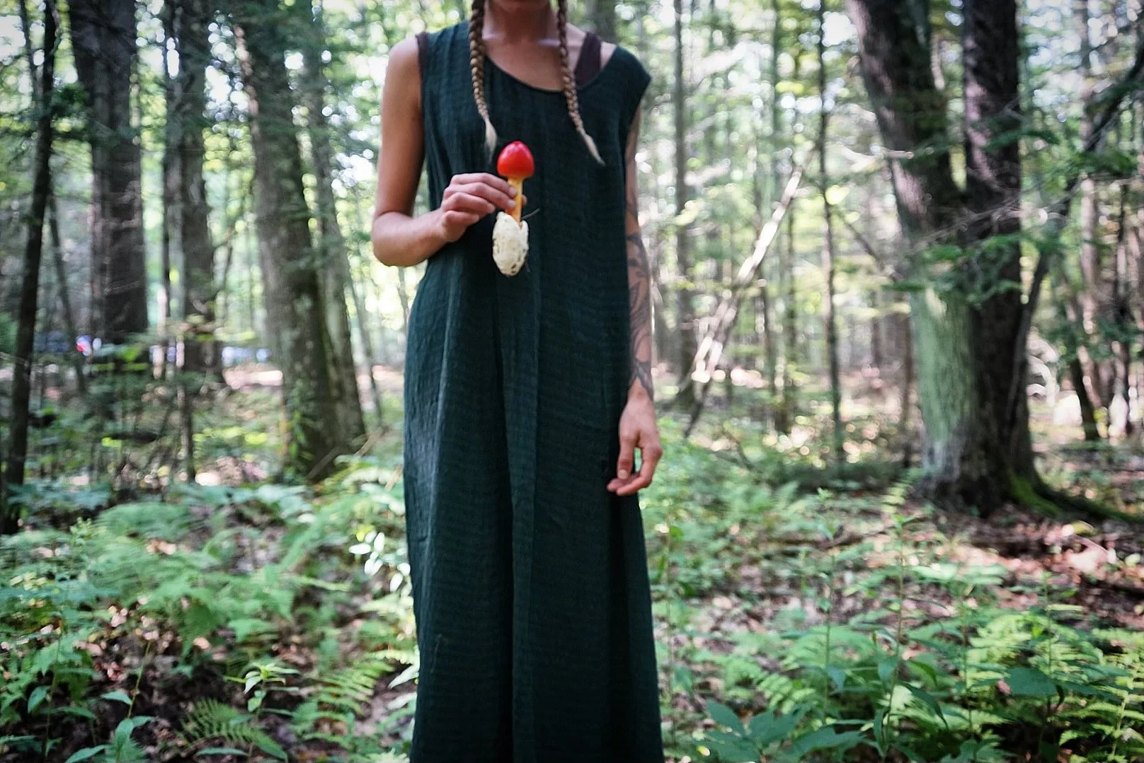 Person standing in a forest holding a mushroom-shaped sculpture.