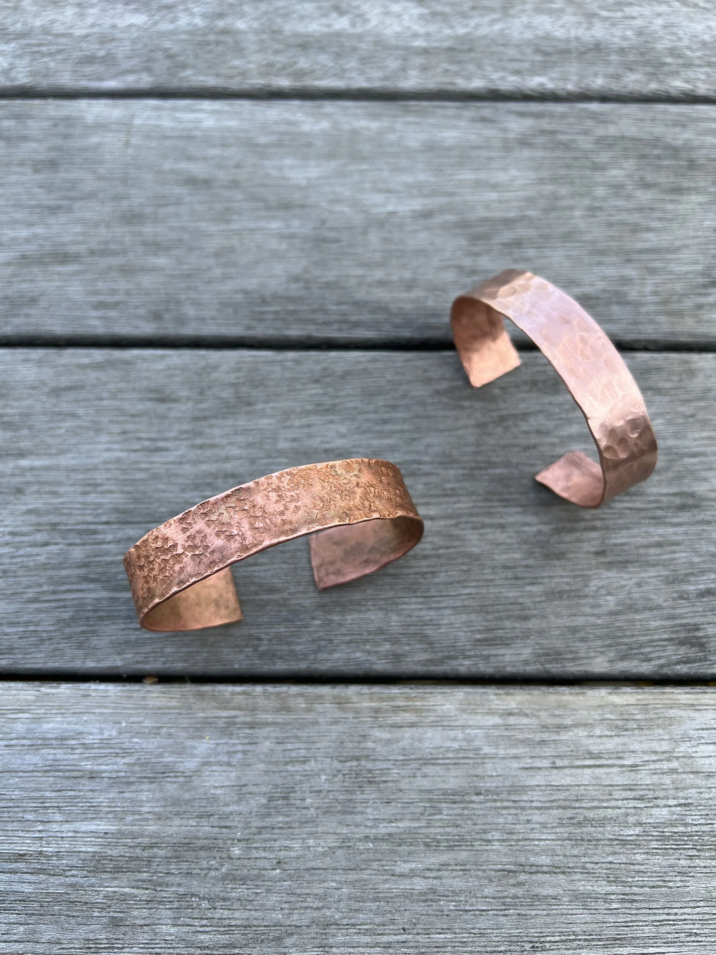 Two hammered copper cuffs on a wooden surface.