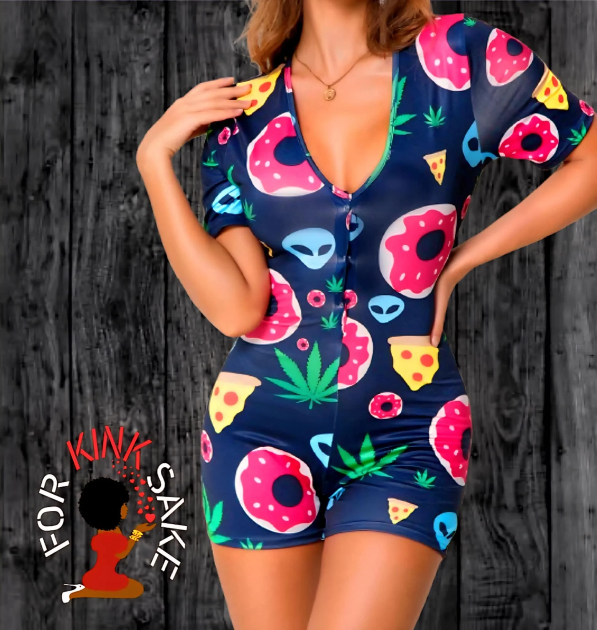 Woman wearing a colorful romper with pizza, donuts, alien faces, cannabis leaves, and pizza slices printed on it, standing against a dark wooden background.