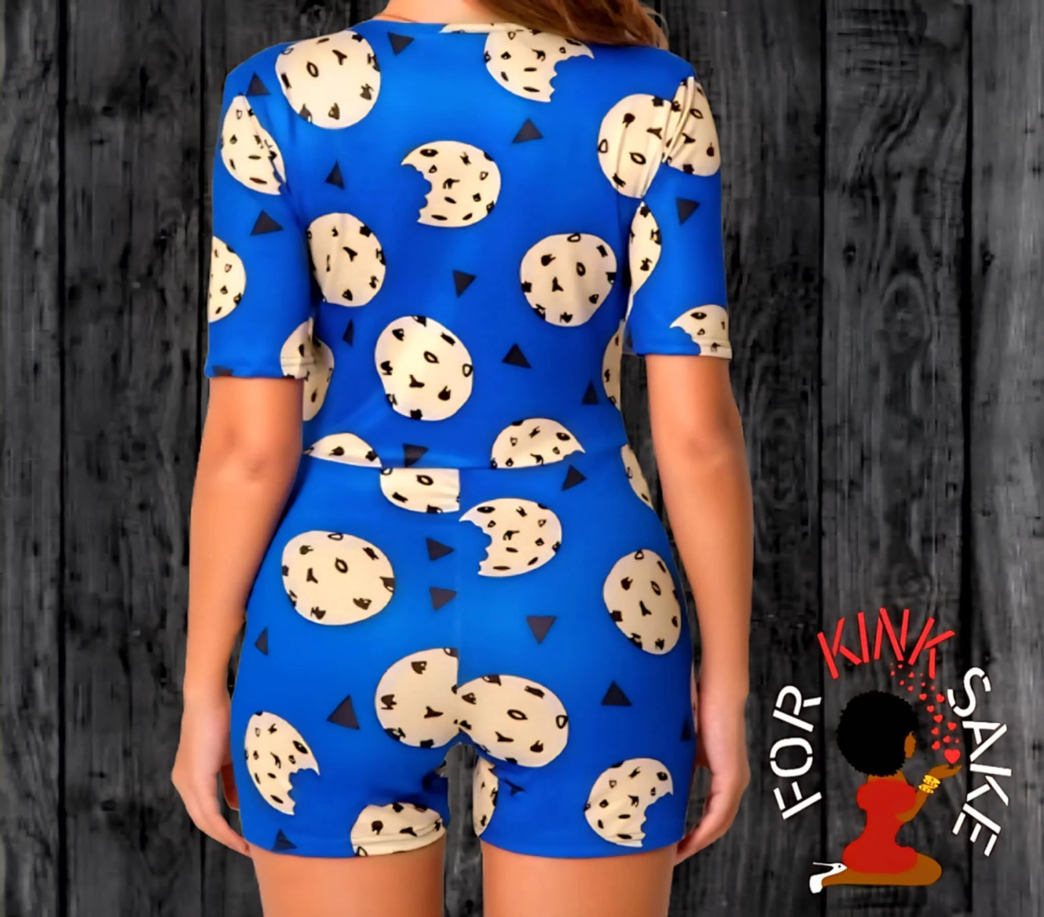 A woman wearing a matching blue shirt and shorts set with a cookie pattern standing in front of a dark wooden wall.
