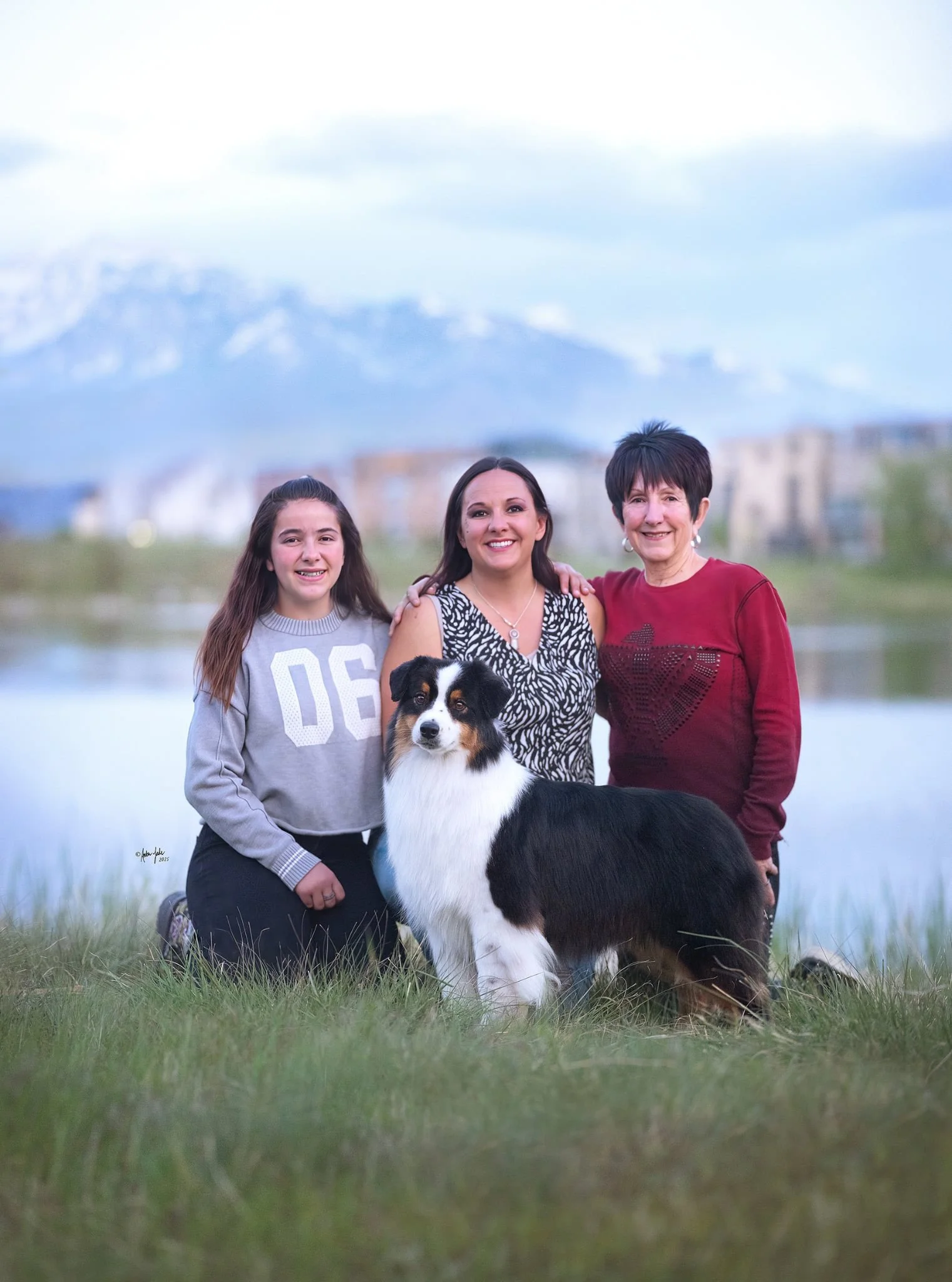 A family of 30-year breeders of Australian Shepherds at Daybreak Lake in Utah with mountains in the background, all smiling and posing with their black tri Australian Shepherd.