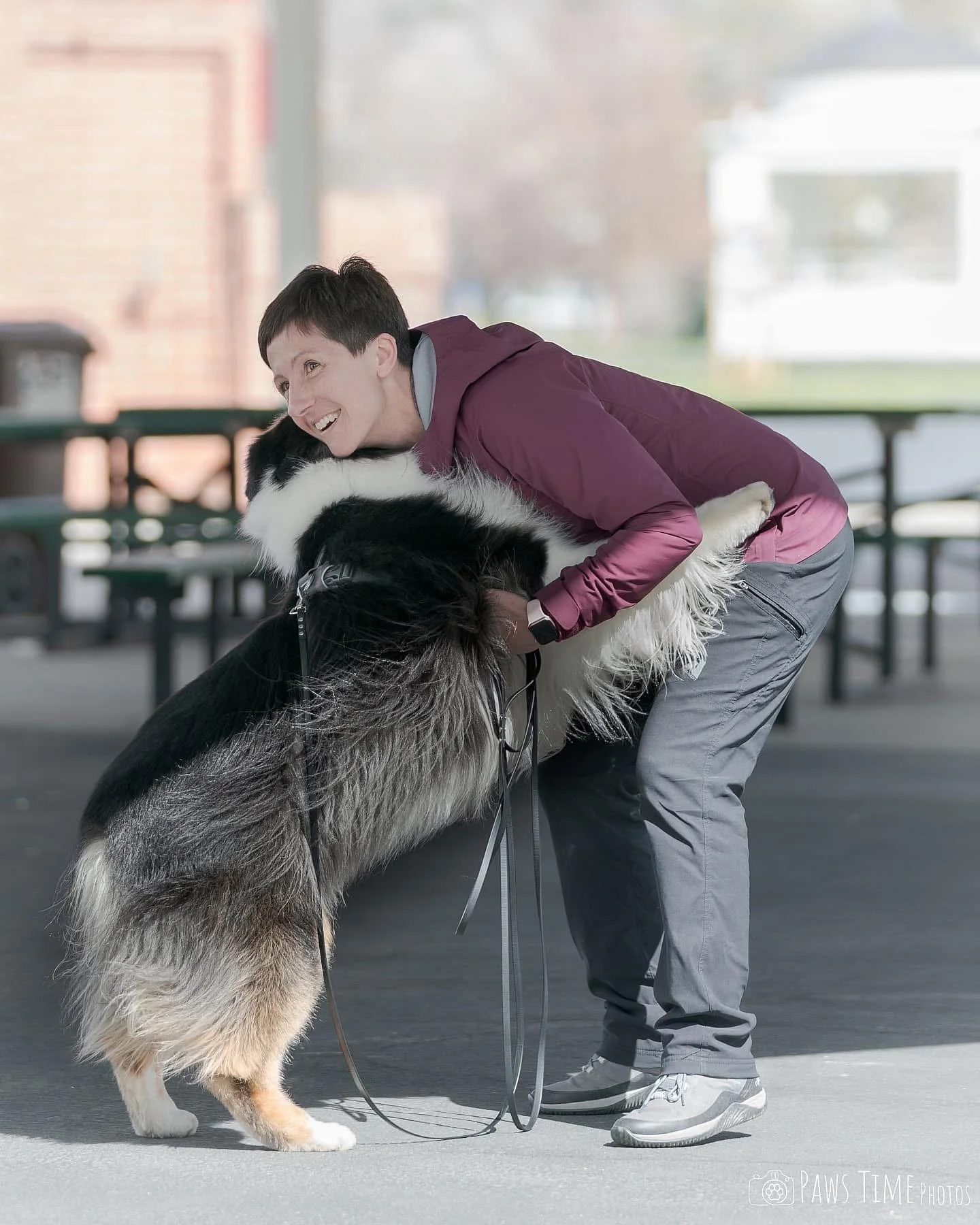 A woman hugging a black tri Australian Shepherd while competing at a scent work or scent detection trial.