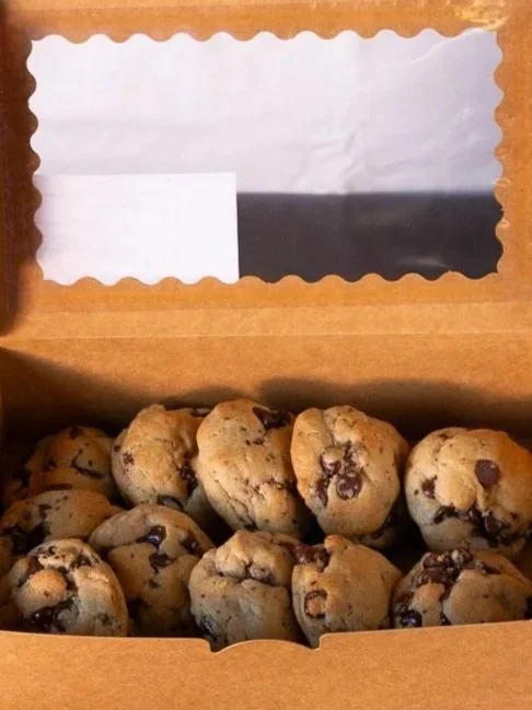 A cardboard box with display window filled with a dozen bakery-style chocolate chip cookies made by a bakery in Spruce View with other baked goods.