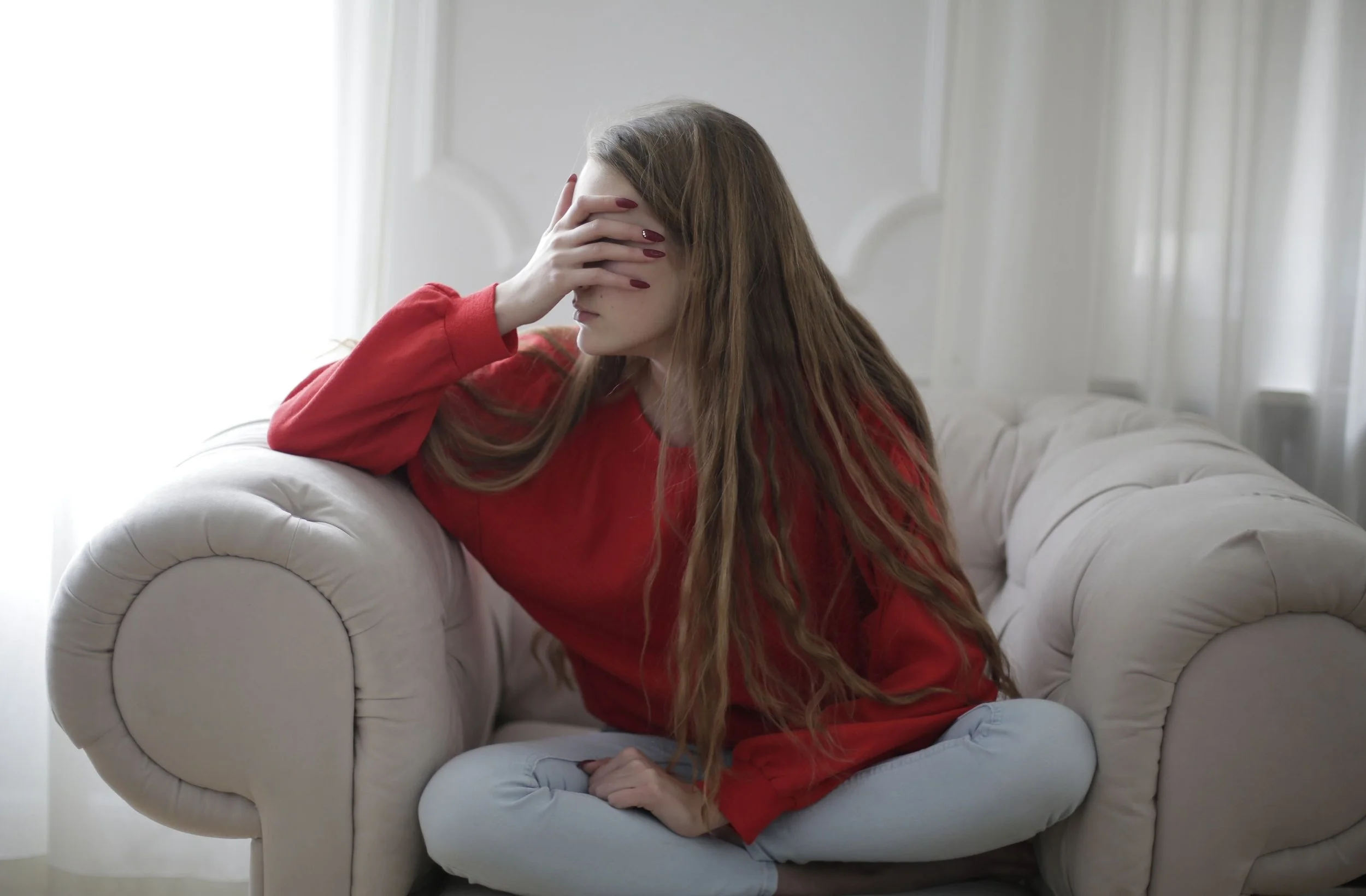 An adult sitting on a couch staring into the distance, illustrating the constant overthinking, restlessness, and mental exhaustion associated with high-functioning anxiety.