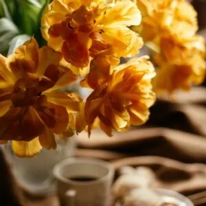 Ramo de flores amarillas sobre una mesa con taza y plato de cerámica.