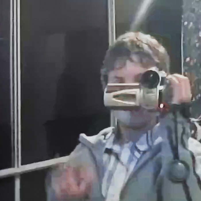 Blake Castle as a young child filming himself waving in the mirror using an old Mini DV tape camcorder.