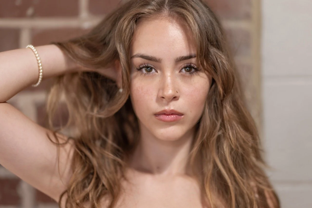 Female model a woman with long, wavy brown hair wearing a white strapless dress, sitting for a portfolio session at Model Muse Studio Fayetteville NC-Model Muse Studio