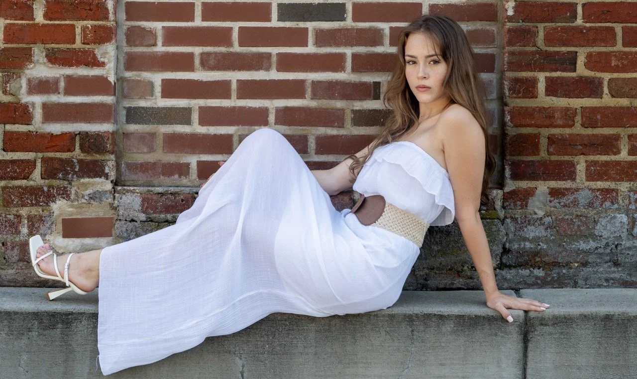 Female model a woman with long, wavy brown hair wearing a white strapless dress, sitting for a portfolio session at Model Muse Studio Fayetteville NC-Model Muse Studio