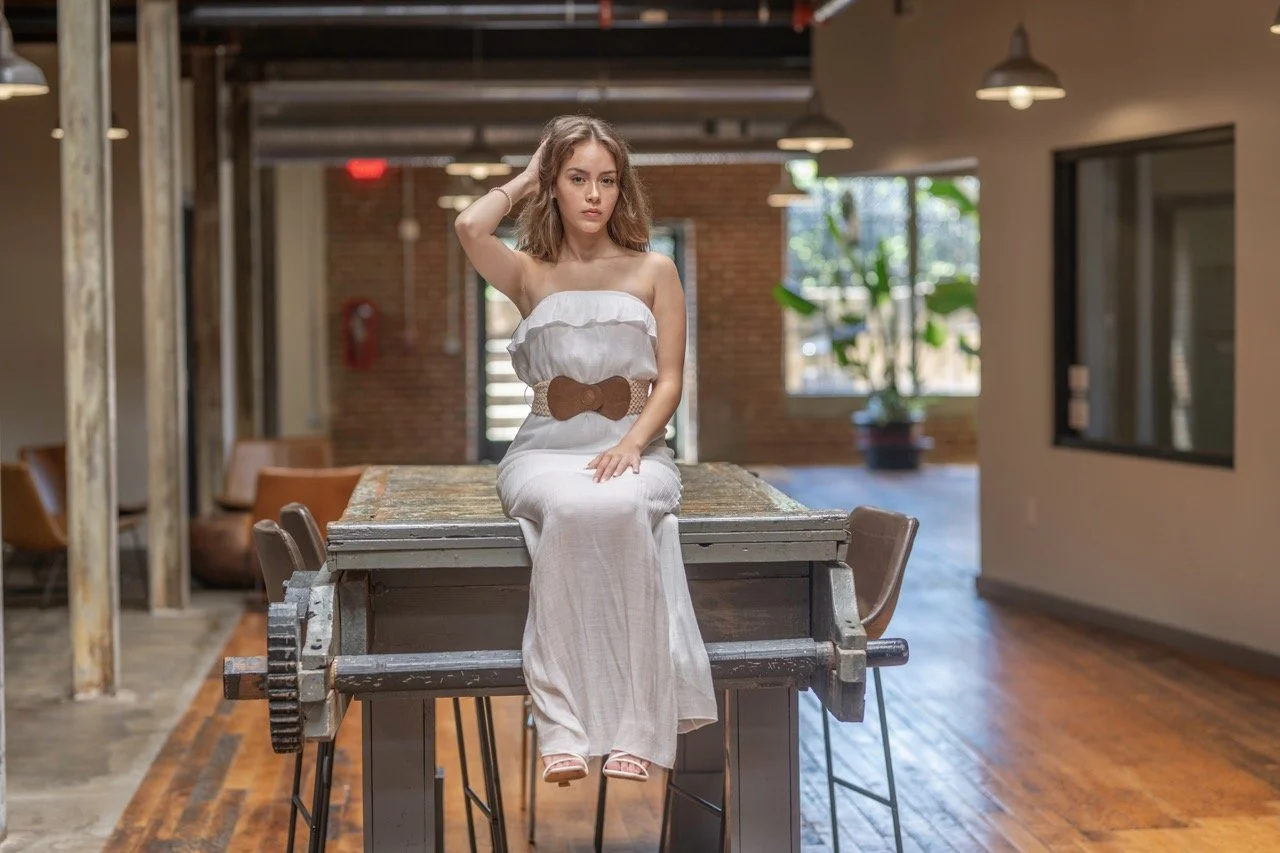 Female model a woman with long, wavy brown hair wearing a white strapless dress, sitting for a portfolio session at Model Muse Studio Fayetteville NC-Model Muse Studio