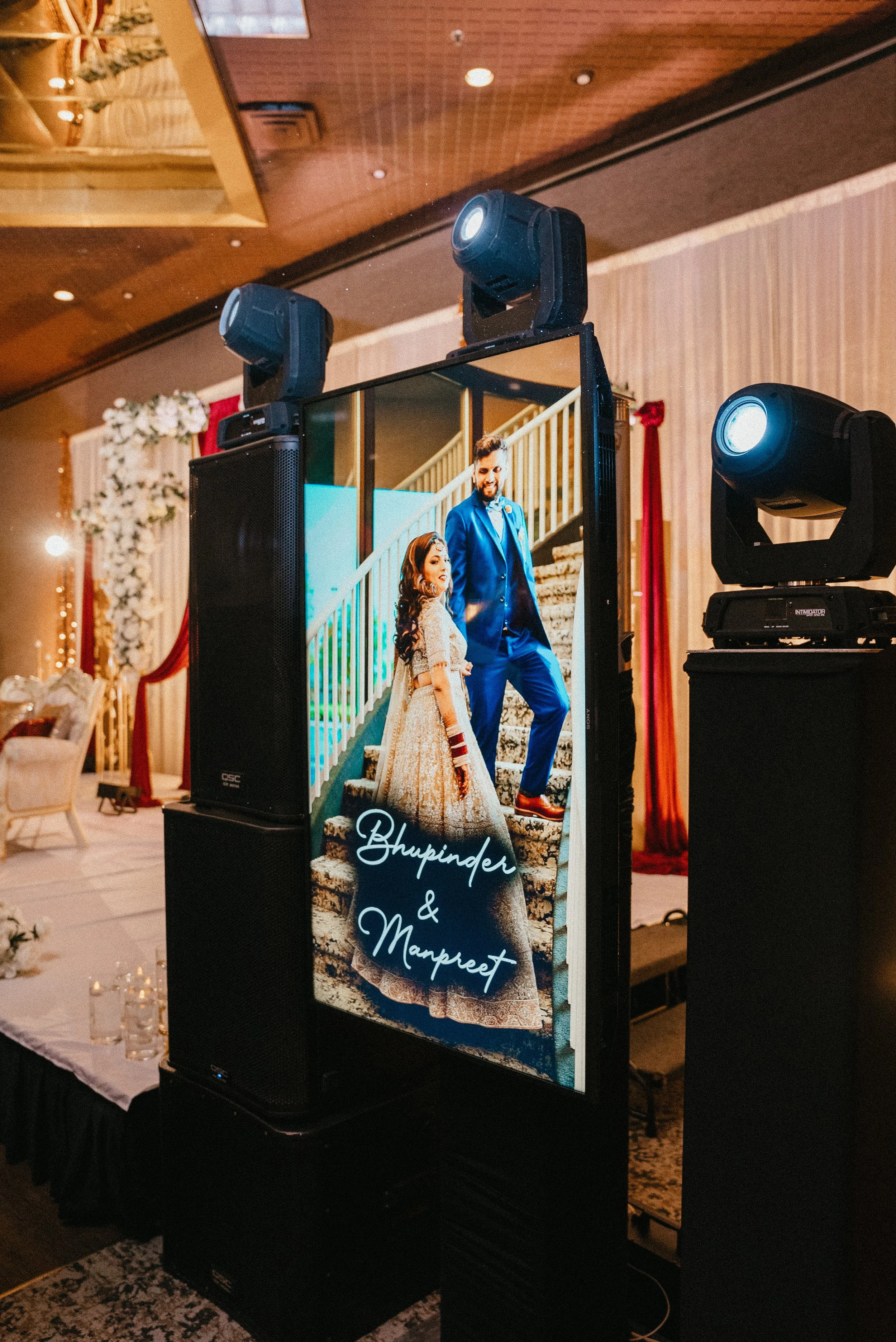 Large digital display screen on a wedding stage showing a bride and groom standing on staircase, with the names Bhupinder and Manpreet written on the screen.