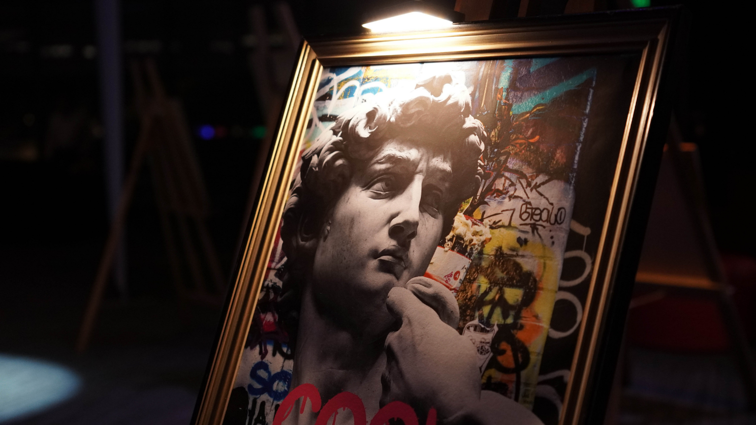 Framed artwork of a classical sculpture head with a hand touching its chin, superimposed on a colorful graffiti background.