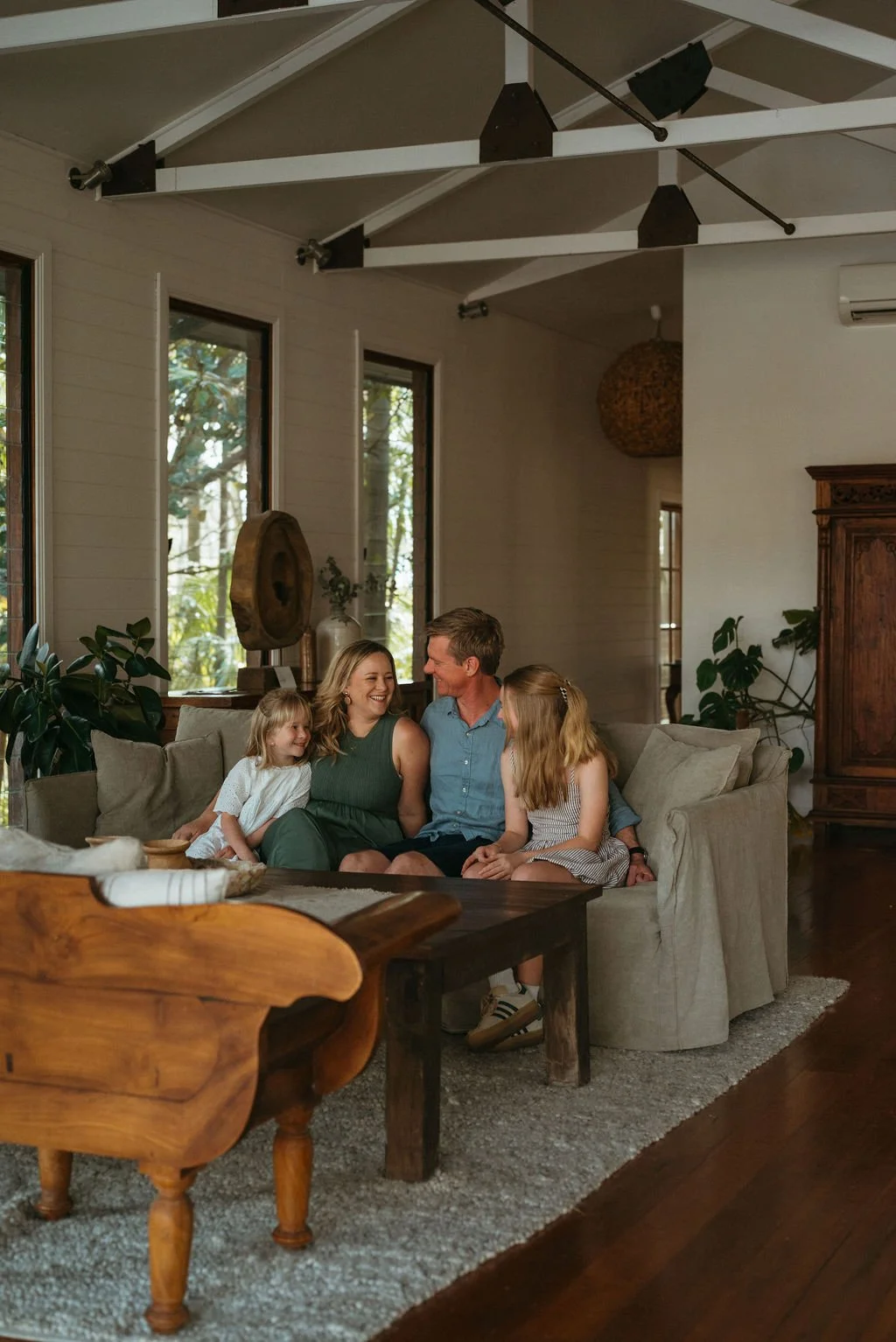 A family of four sitting on a sofa in a living room, smiling and laughing together at Leaves and Fishes Villa