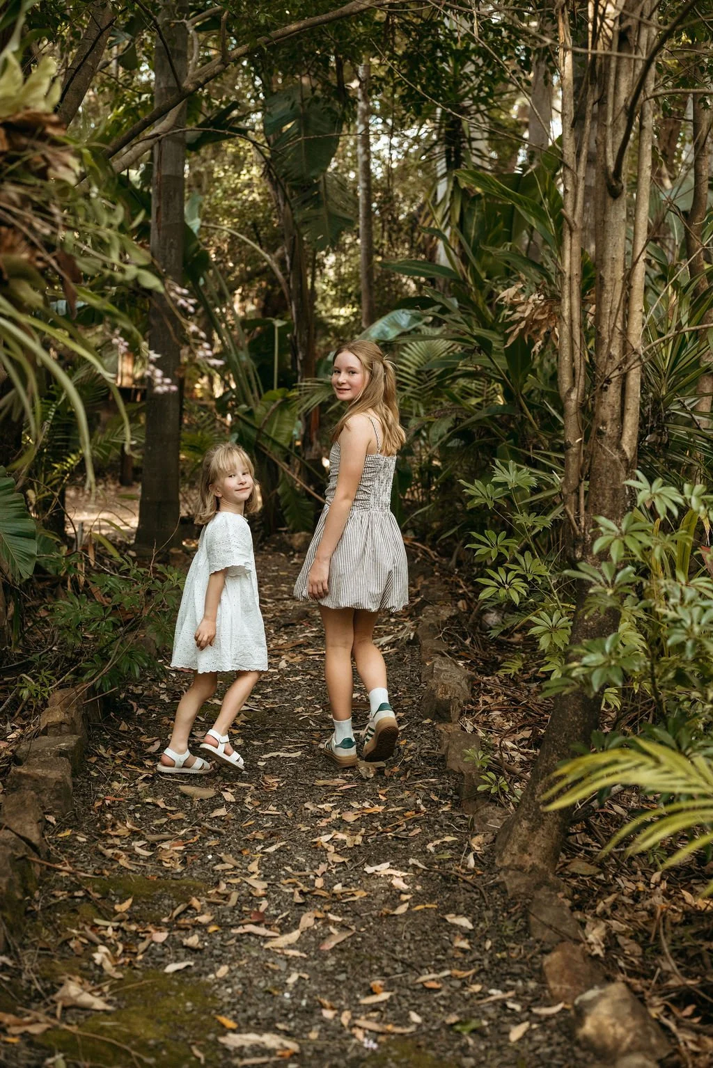 Two sisters walking together along a lush forest path surrounded by greenery at Secret Garden