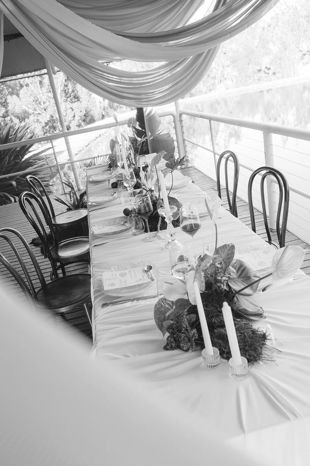 Table set with candles, wine glasses, and a floral centerpiece on a decorated outdoor patio with draped fabric overhead.