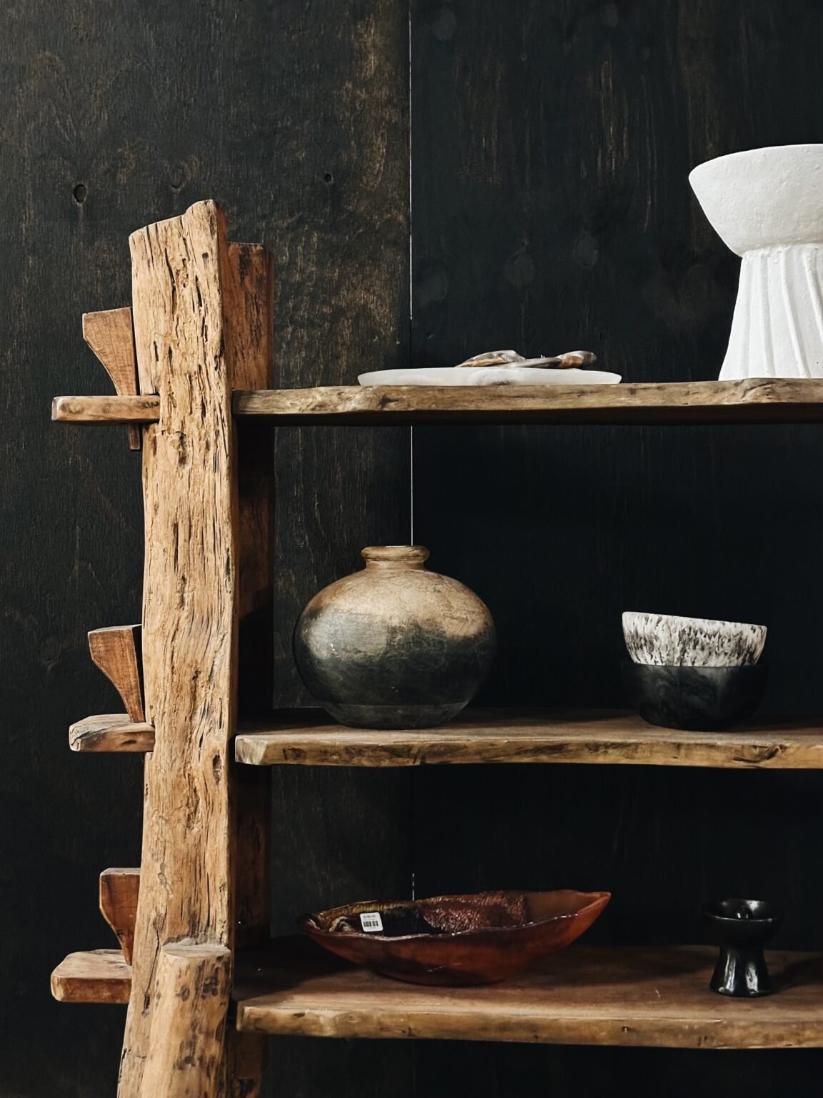 A rustic wooden shelf with three tiers displaying ceramic and wooden bowls and vases against a dark background at The Trove Homewares