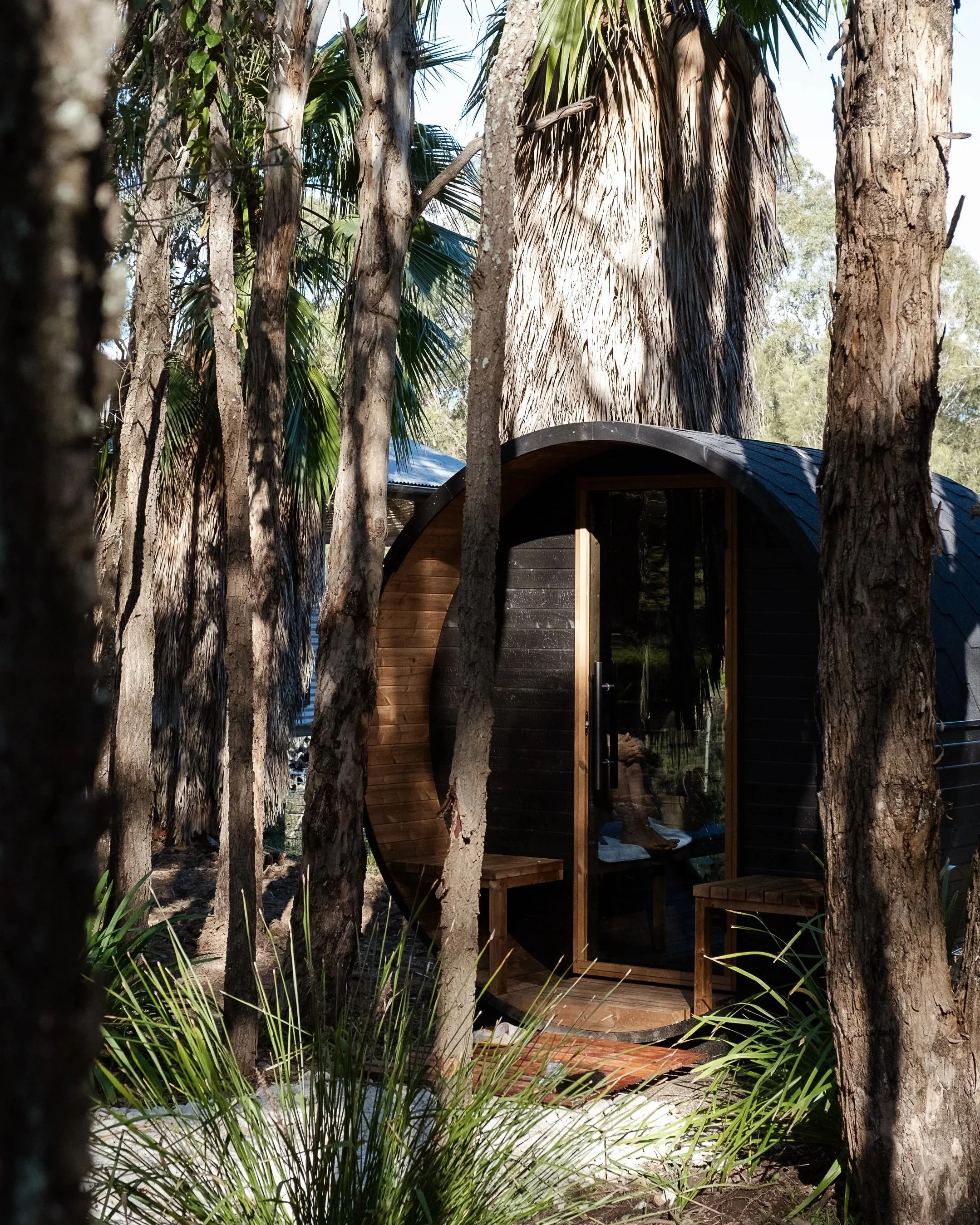 outdoor barrel sauna nestled in trees at leaves and fishes