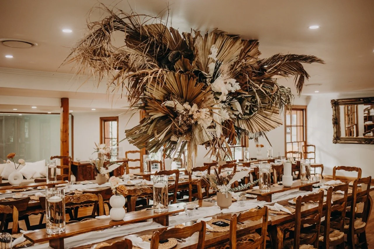 Indoor wedding venue with long wooden tables and large dried floral centerpieces at Leaves and Fishes