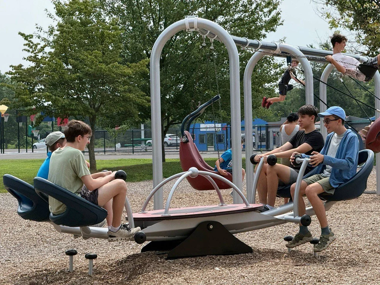 Children playing on a multi-person see-saw at a playground, with some kids swinging and others sitting.