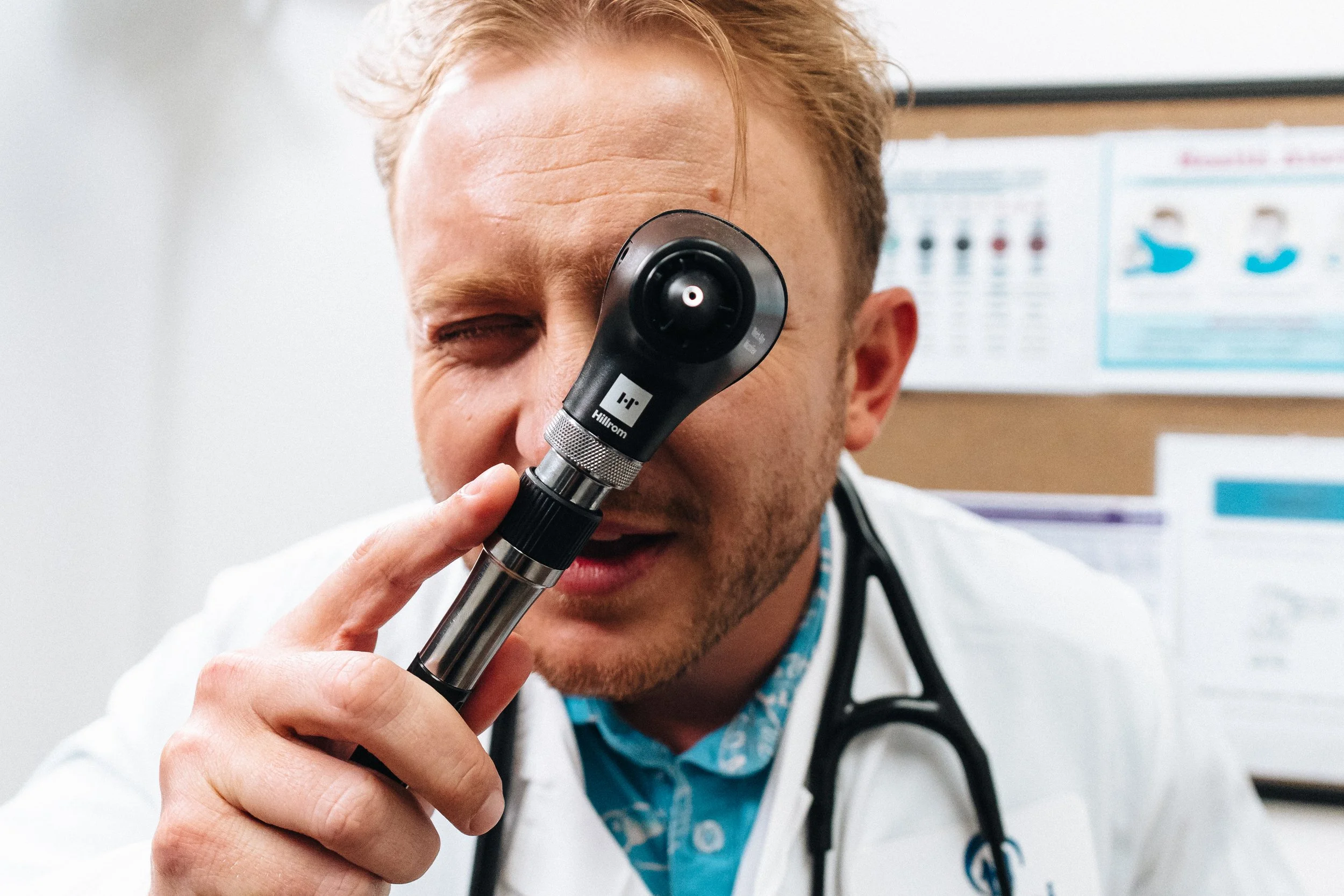 A male doctor using an otoscope to examine the patient's ear in a medical office.