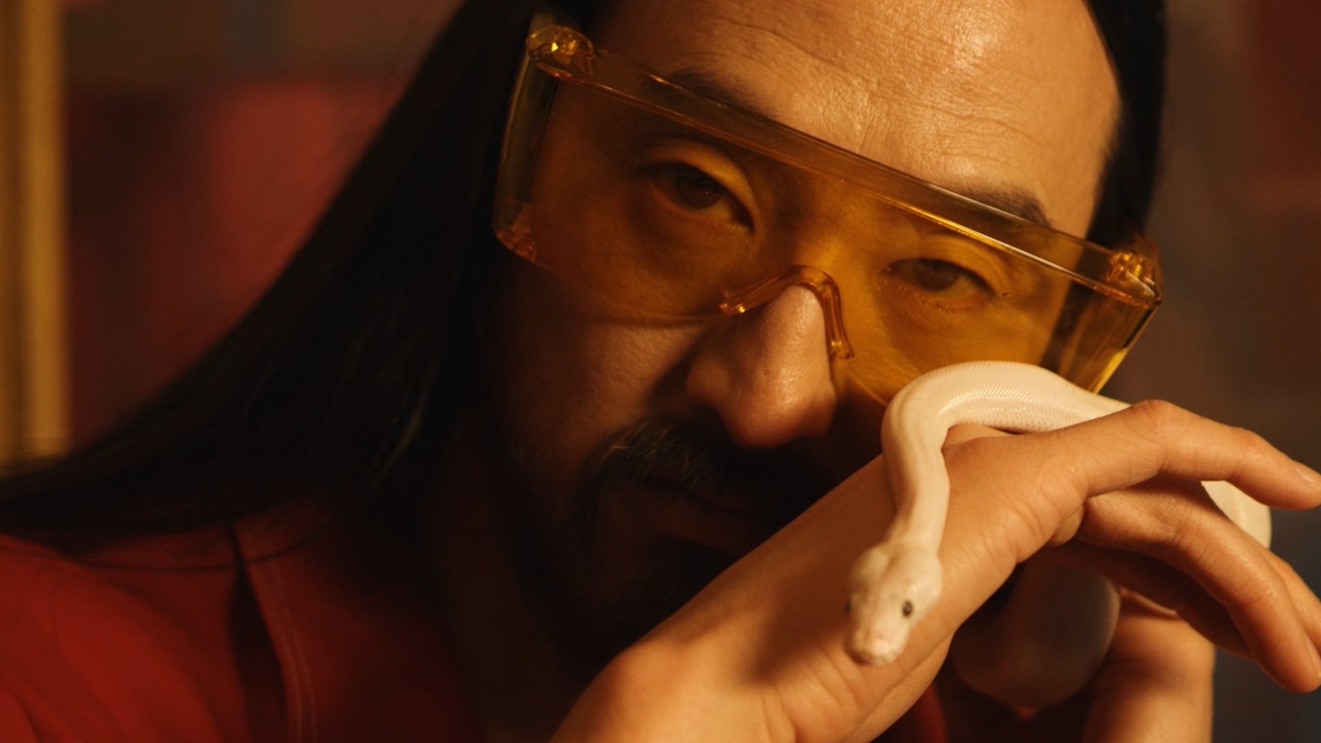 A person wearing orange-tinted safety glasses is holding and smelling a white python.