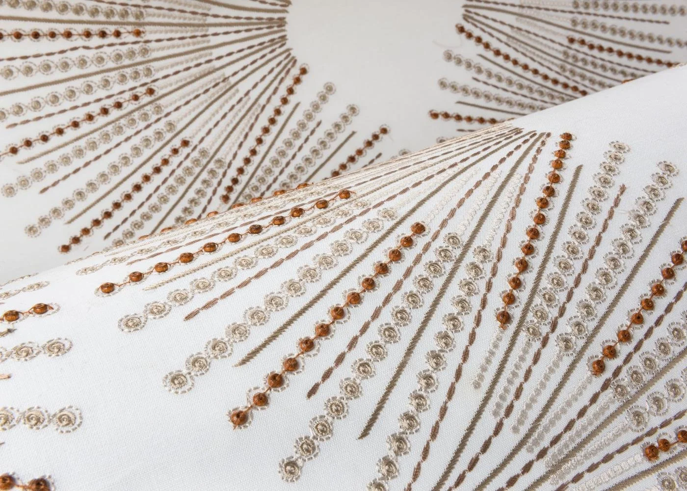 Fabric with intricate embroidery of parallel lines and small circular embellishments in shades of gold and bronze on a white background.