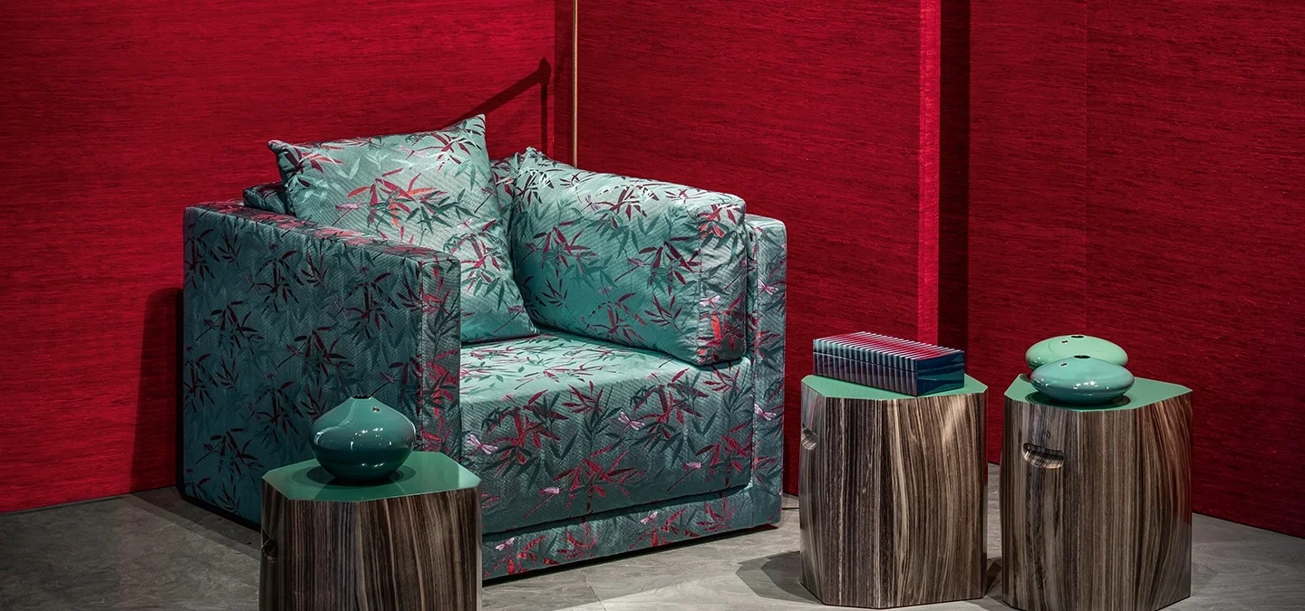 Modern seating area with patterned armchair, decorative vases, and books, against red textured wall.
