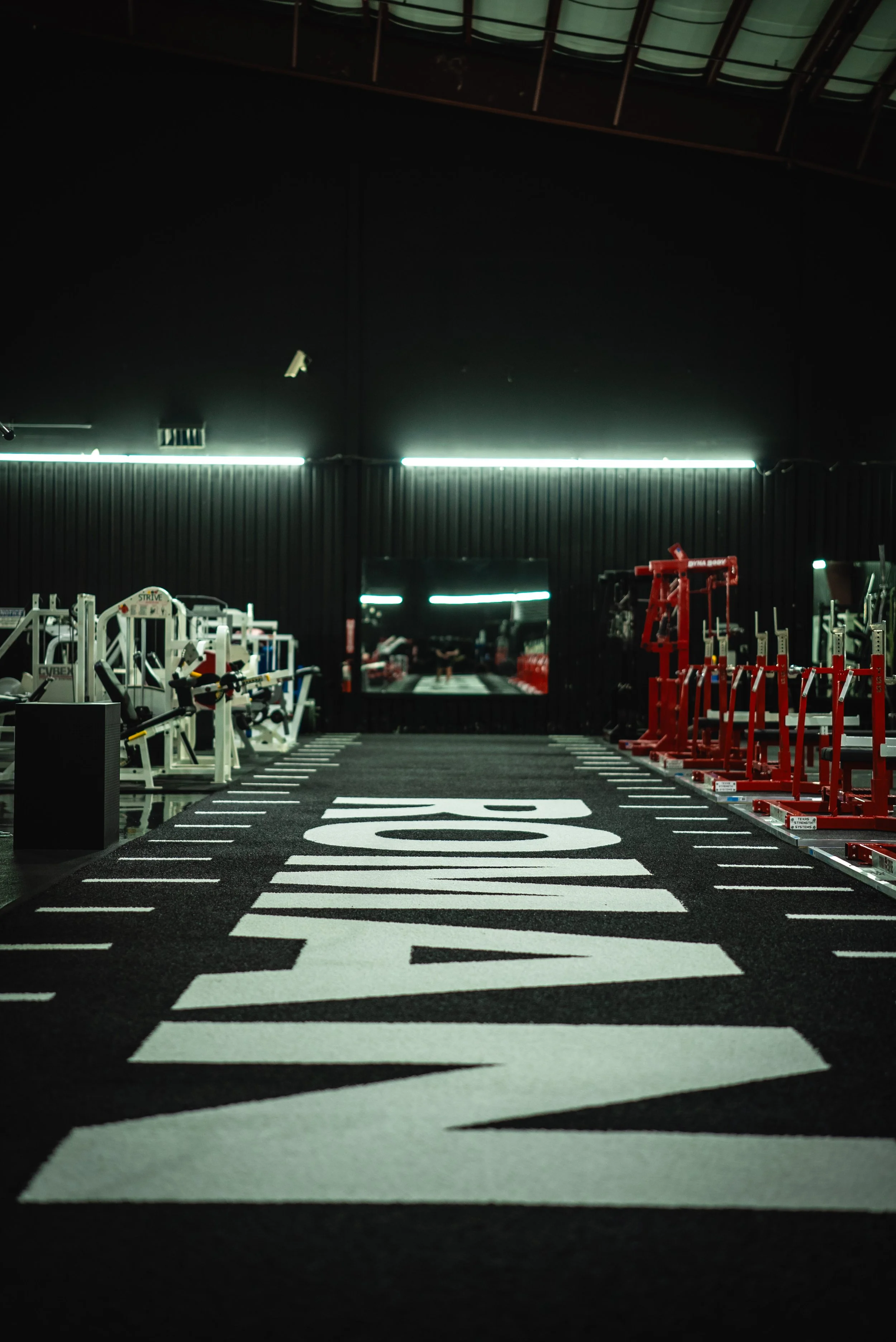 Empty gym with a running track in the center, fitness equipment on the left, red weights on the right, and a large mirror at the back reflecting the interior.