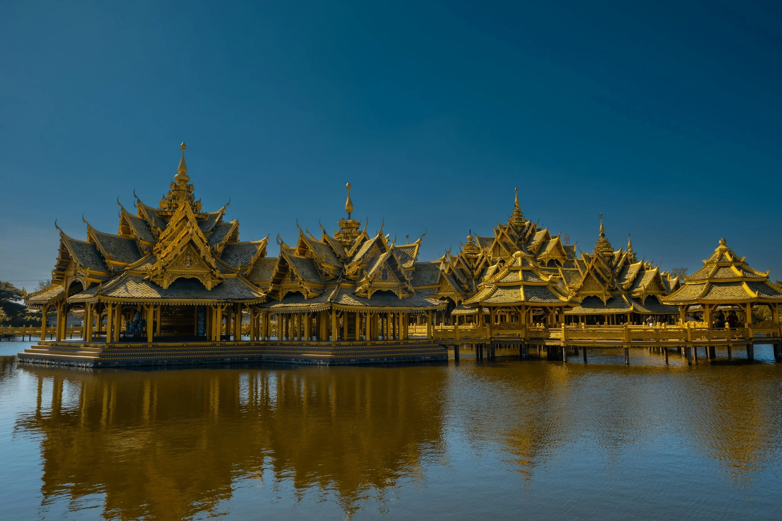 A gold-colored traditional Thai-style building on stilts over water, with a blue sky background.