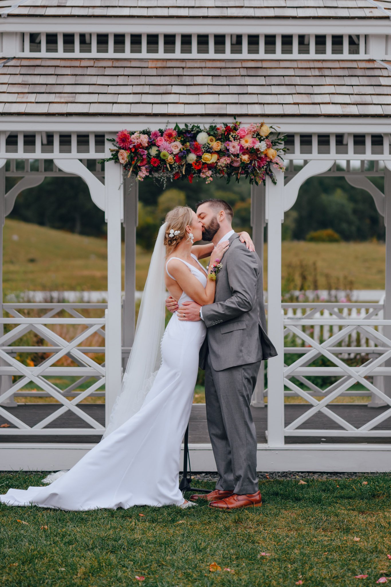 Bride and groom kissing under a floral arch at their wedding in an outdoor garden.