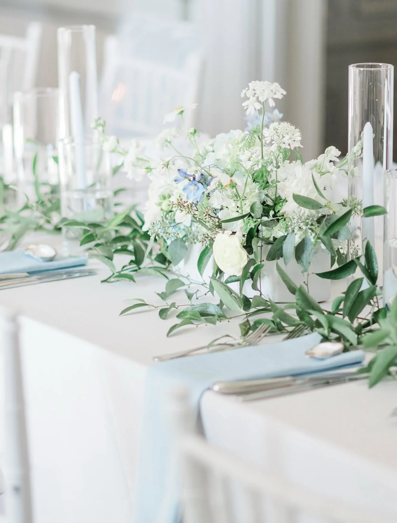 Elegant table setting with a white floral centerpiece, glassware, and silverware on a white tablecloth.