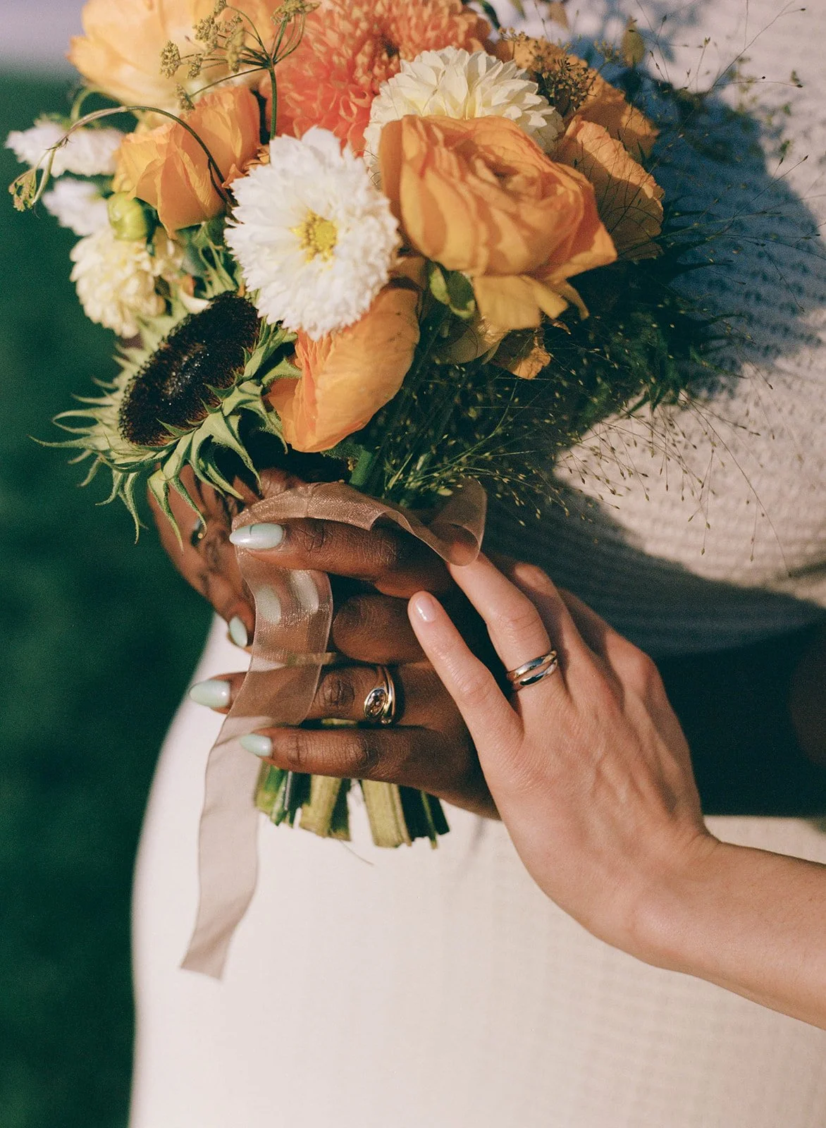 A person holding a bouquet of mixed flowers with hands adorned with rings and light-colored nail polish.