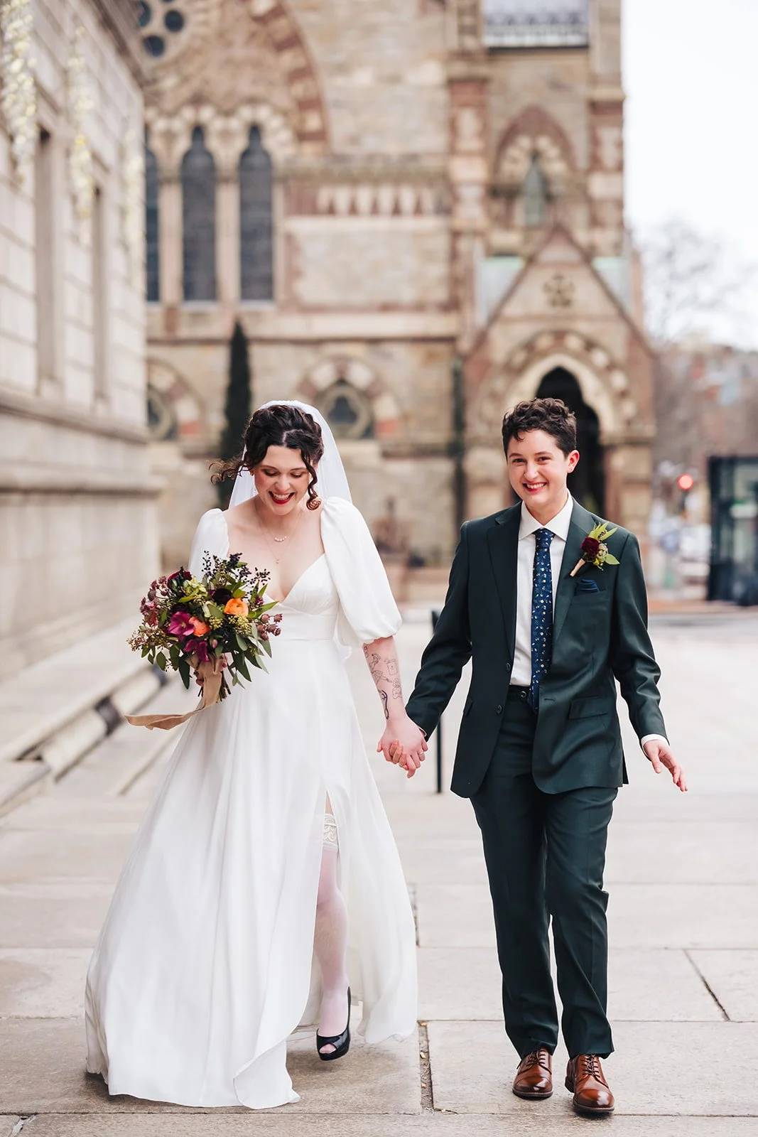 A bride and groom holding hands and smiling as they walk outside a church