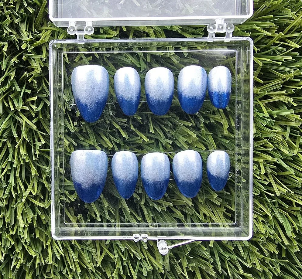 A transparent case with 10 blue and white ombre nails on a green grass background.