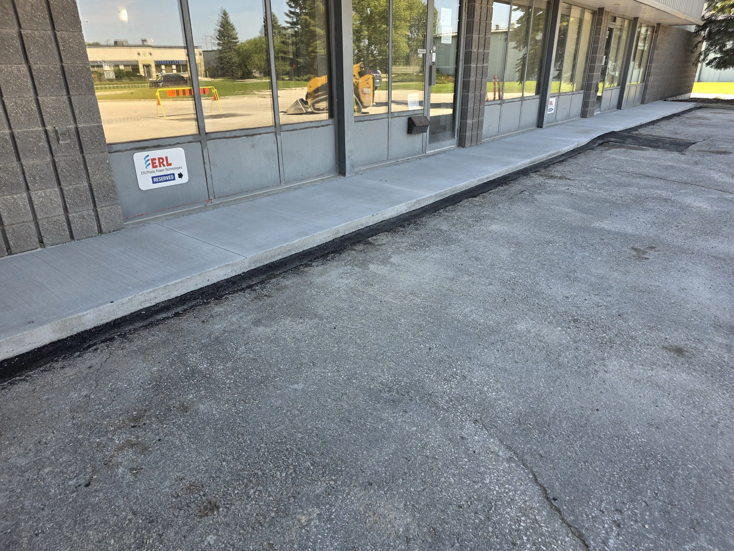 Empty parking lot with a newly paved sidewalk outside a commercial building with large glass windows and a sign indicating reserved parking for ERL EPIS Power Technologies.