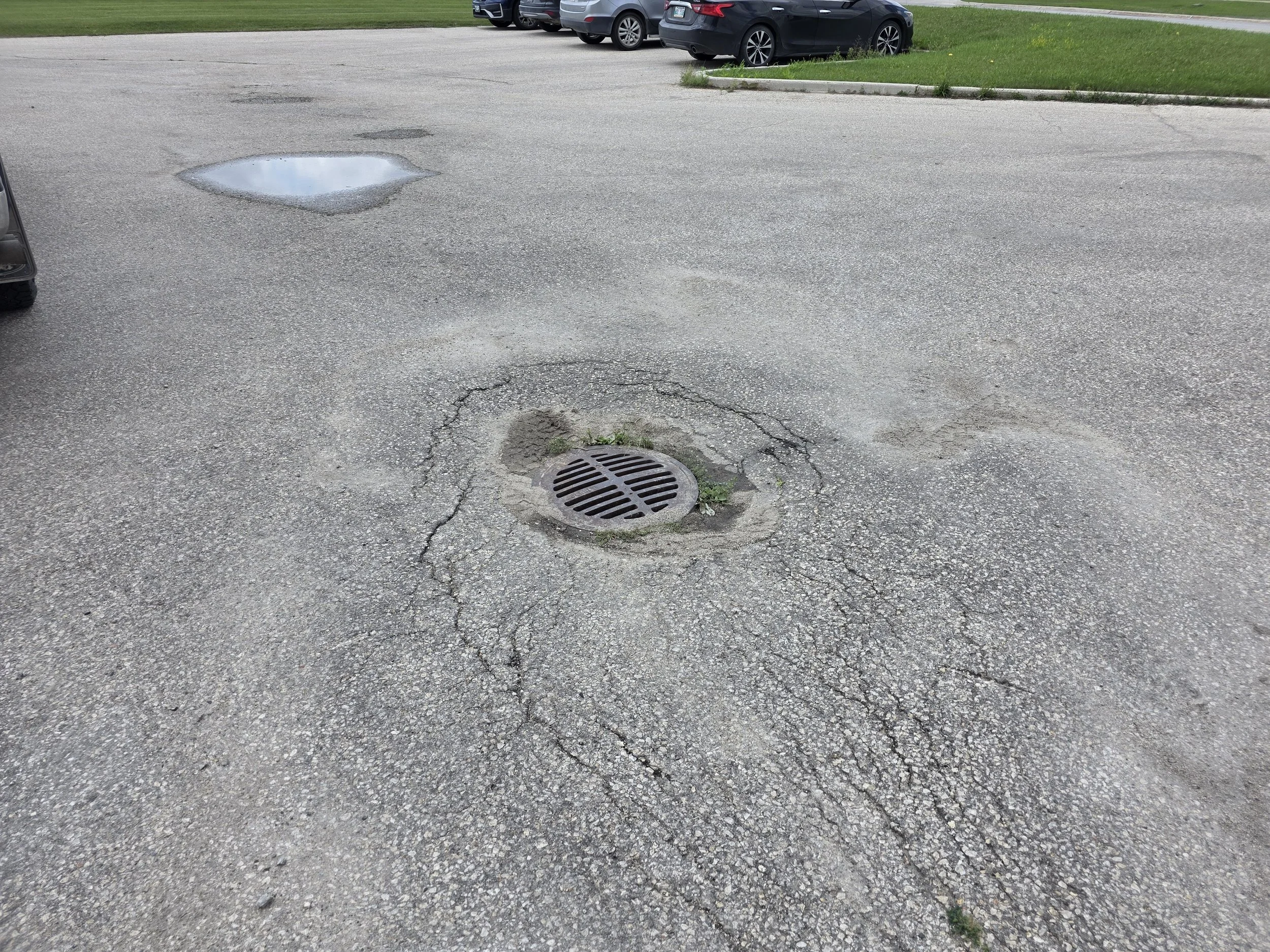 Parking lot pavement with a manhole / drain surrounded by cracked asphalt.