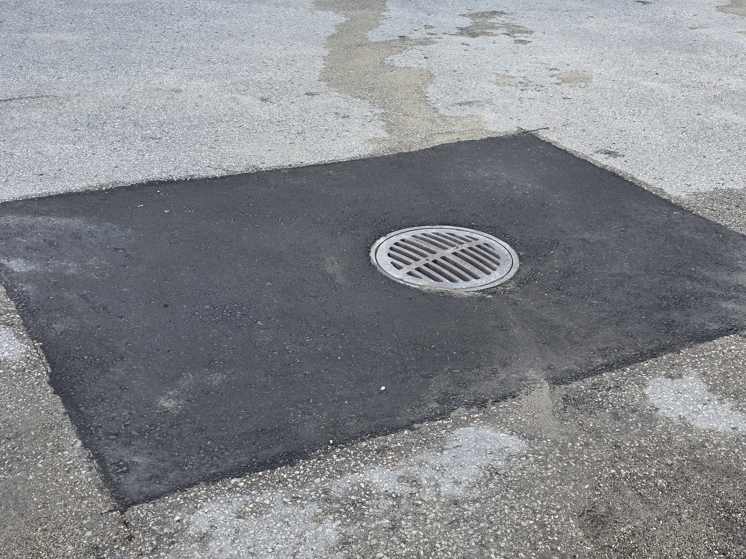 A freshly paved section of parking lot with a manhole / drain in the center.
