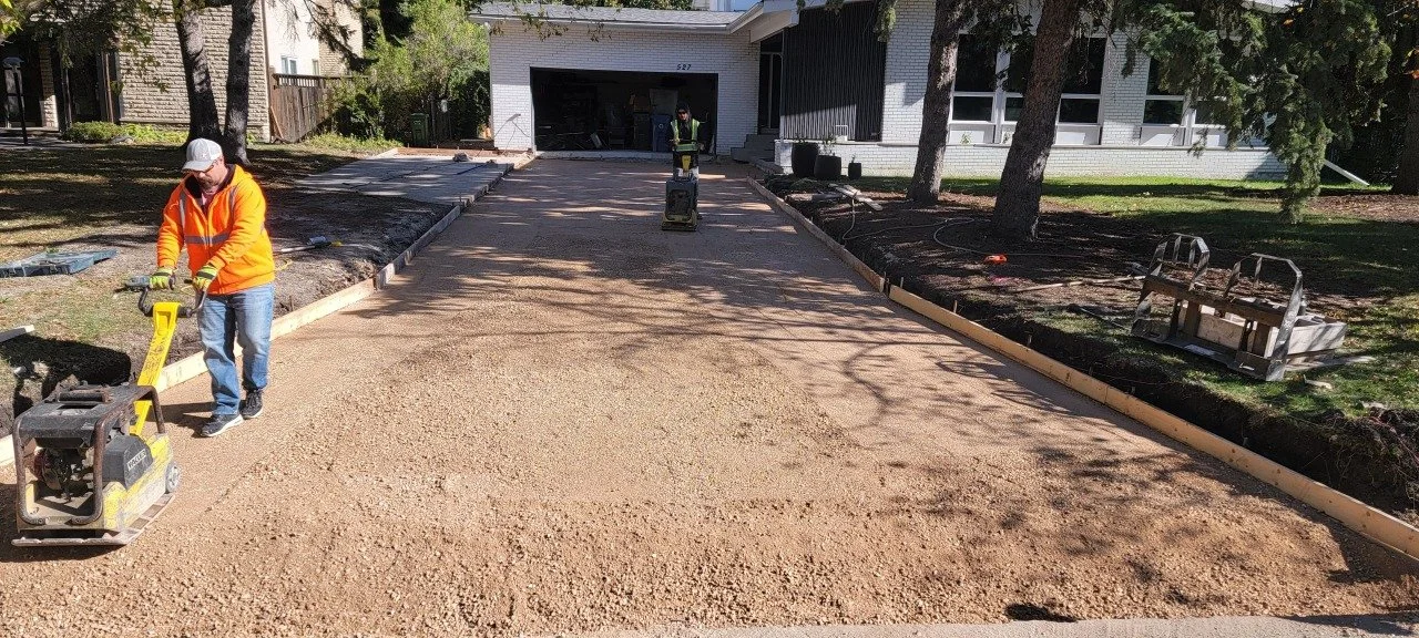 Construction workers leveling gravel on a driveway in front of a house.