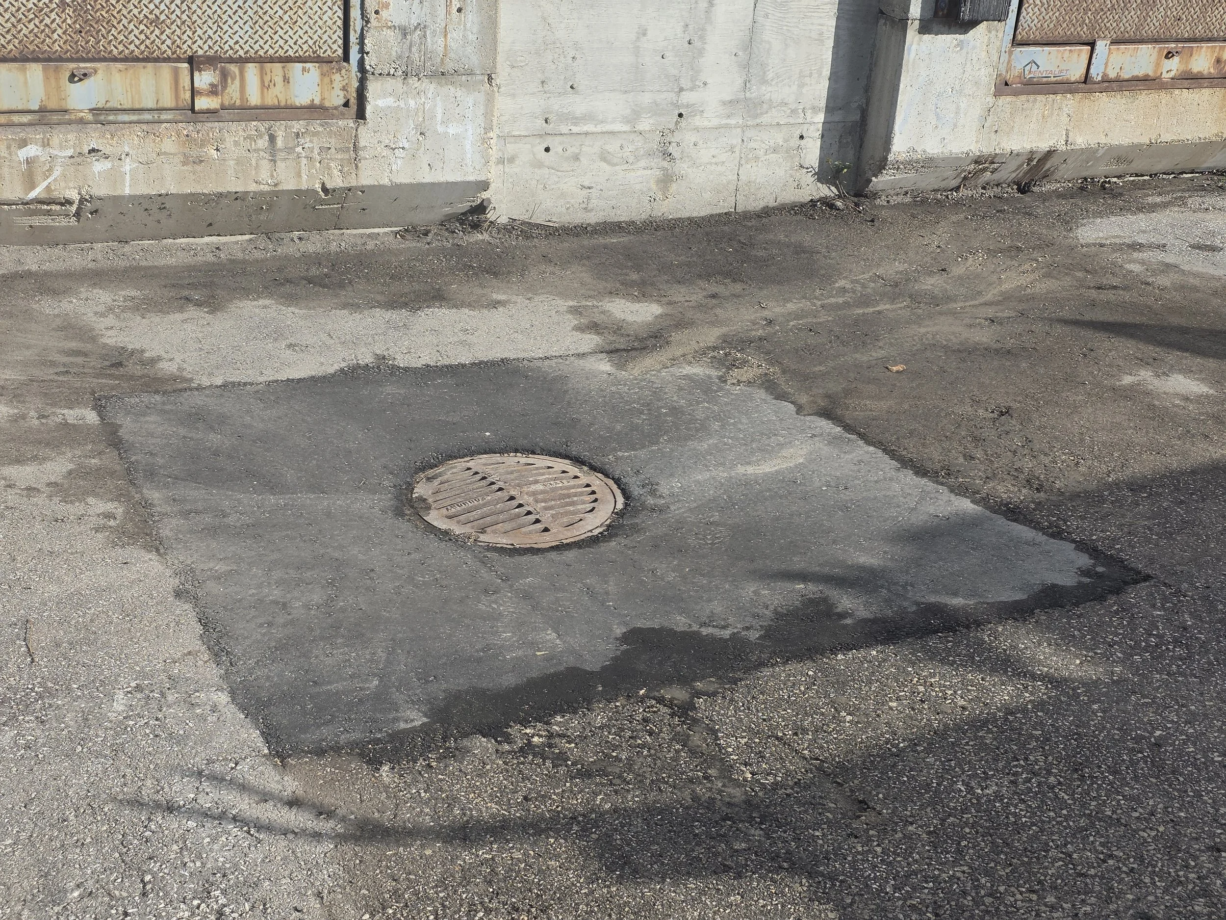 A freshly paved section of parking lot with a manhole / drain in the center.